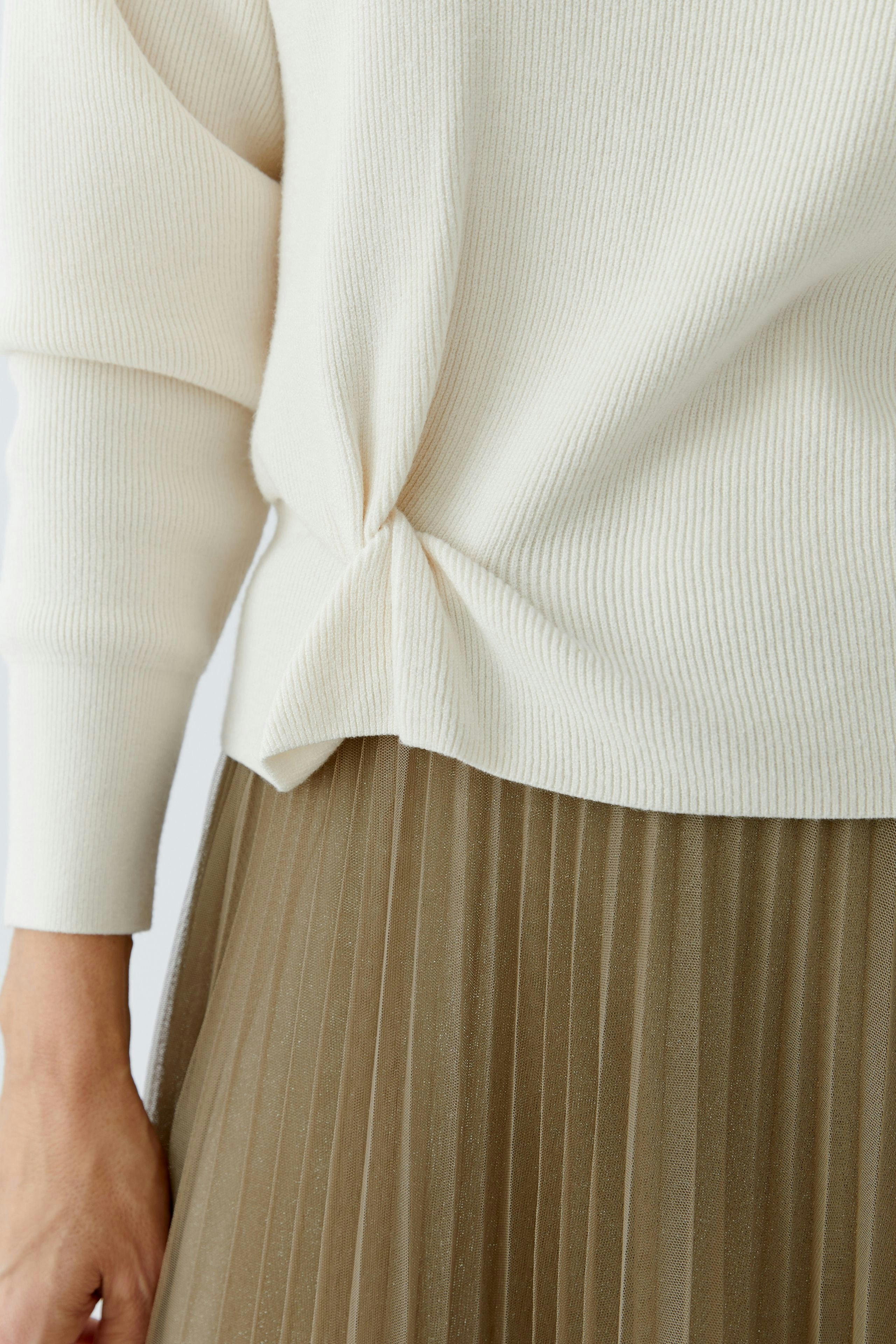 Casual women's pullover: Close-up of a woman in a cream ribbed pullover, styled with a pleated skirt.