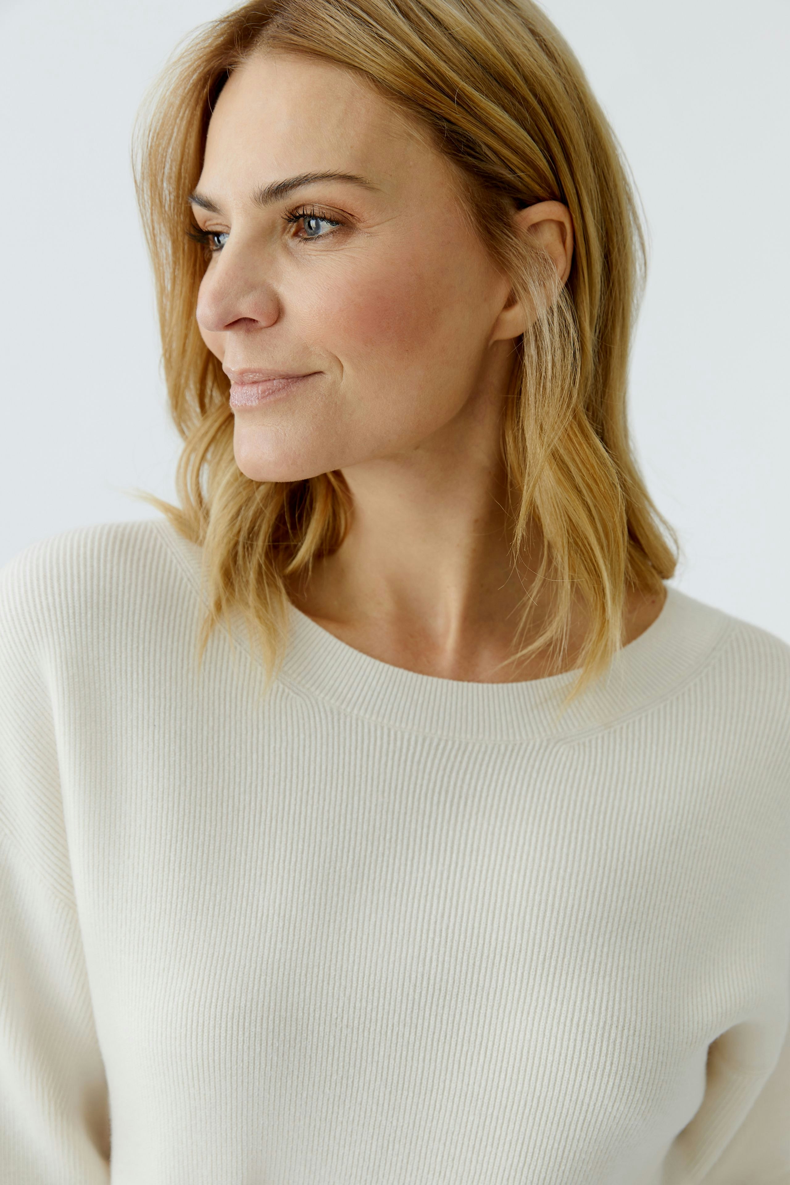 Casual women's pullover: Woman in a soft cream ribbed pullover with a relaxed fit, looking content.