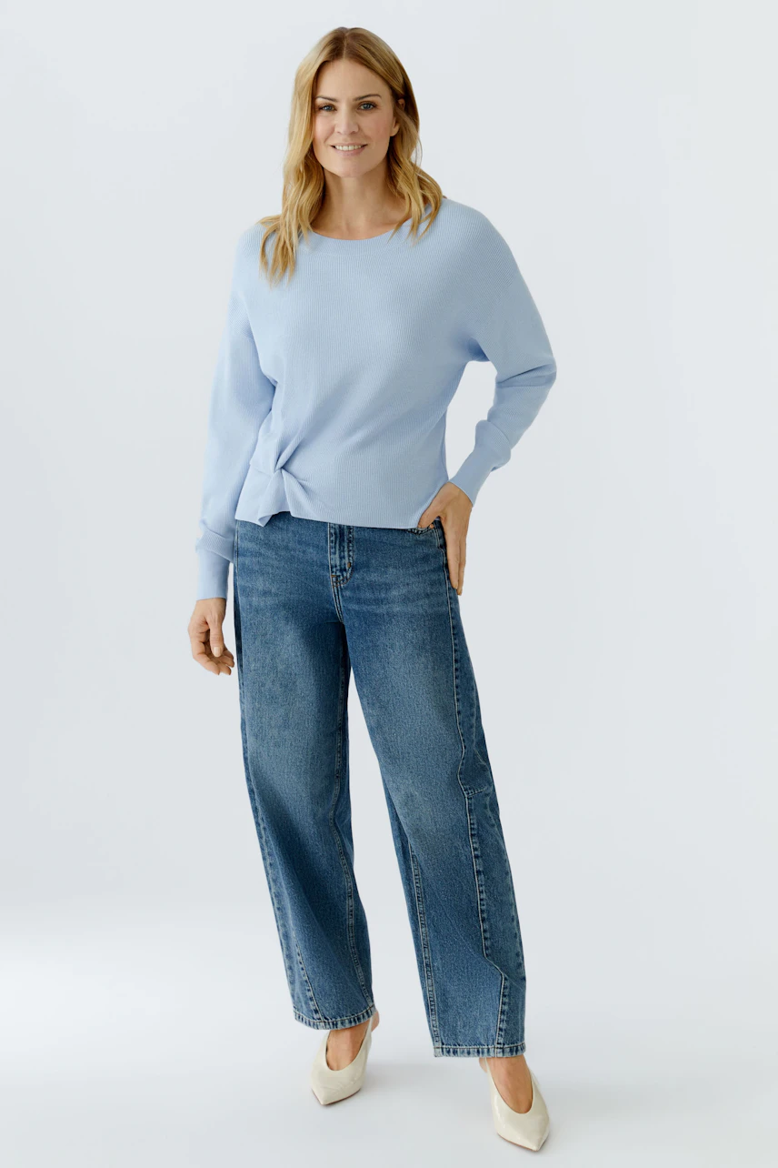 Casual women's pullover: Woman in a light blue pullover paired with wide-leg jeans, smiling confidently.