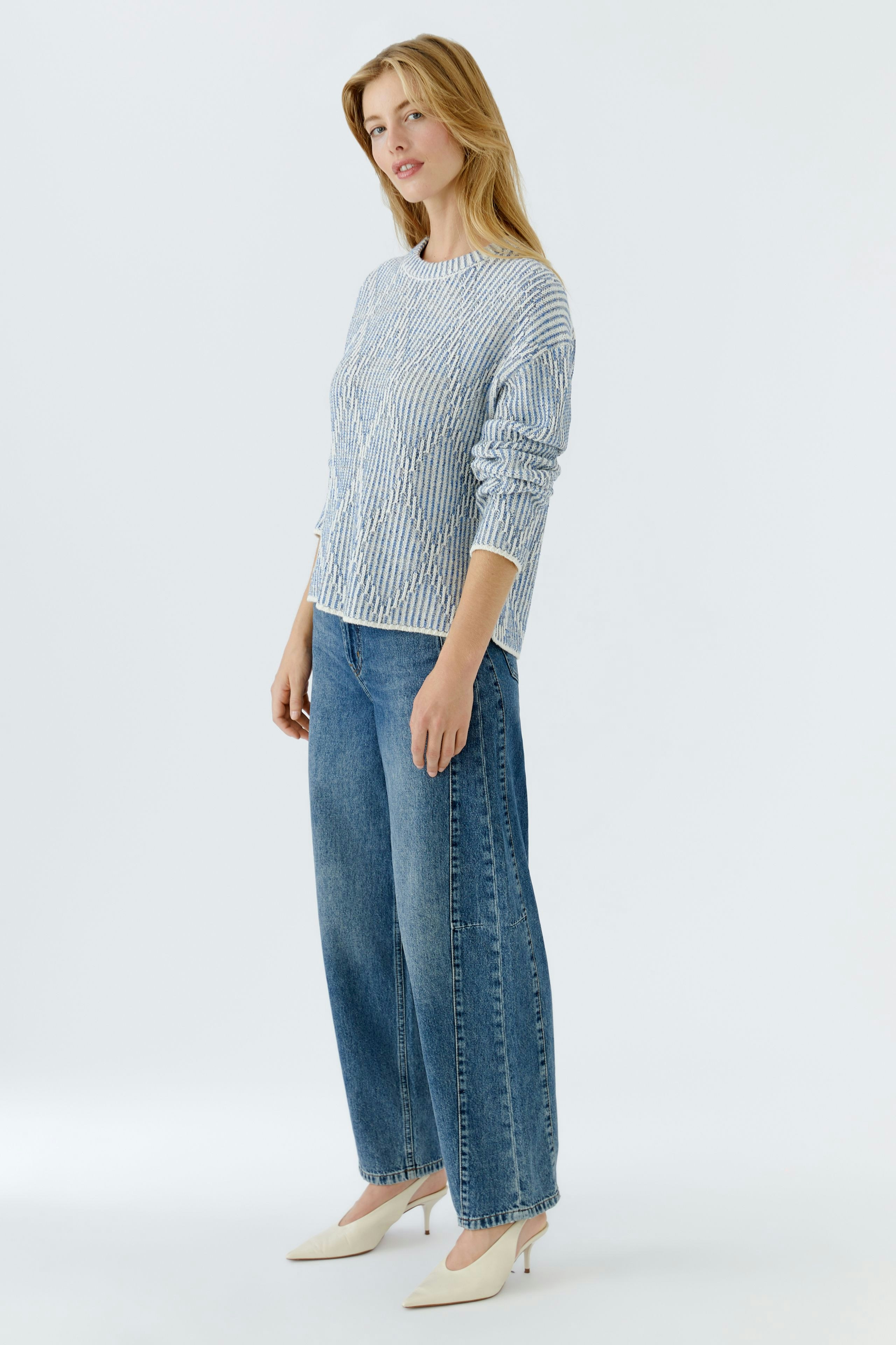 Casual women's pullover: Young woman in a striped pullover paired with wide jeans, standing confidently.