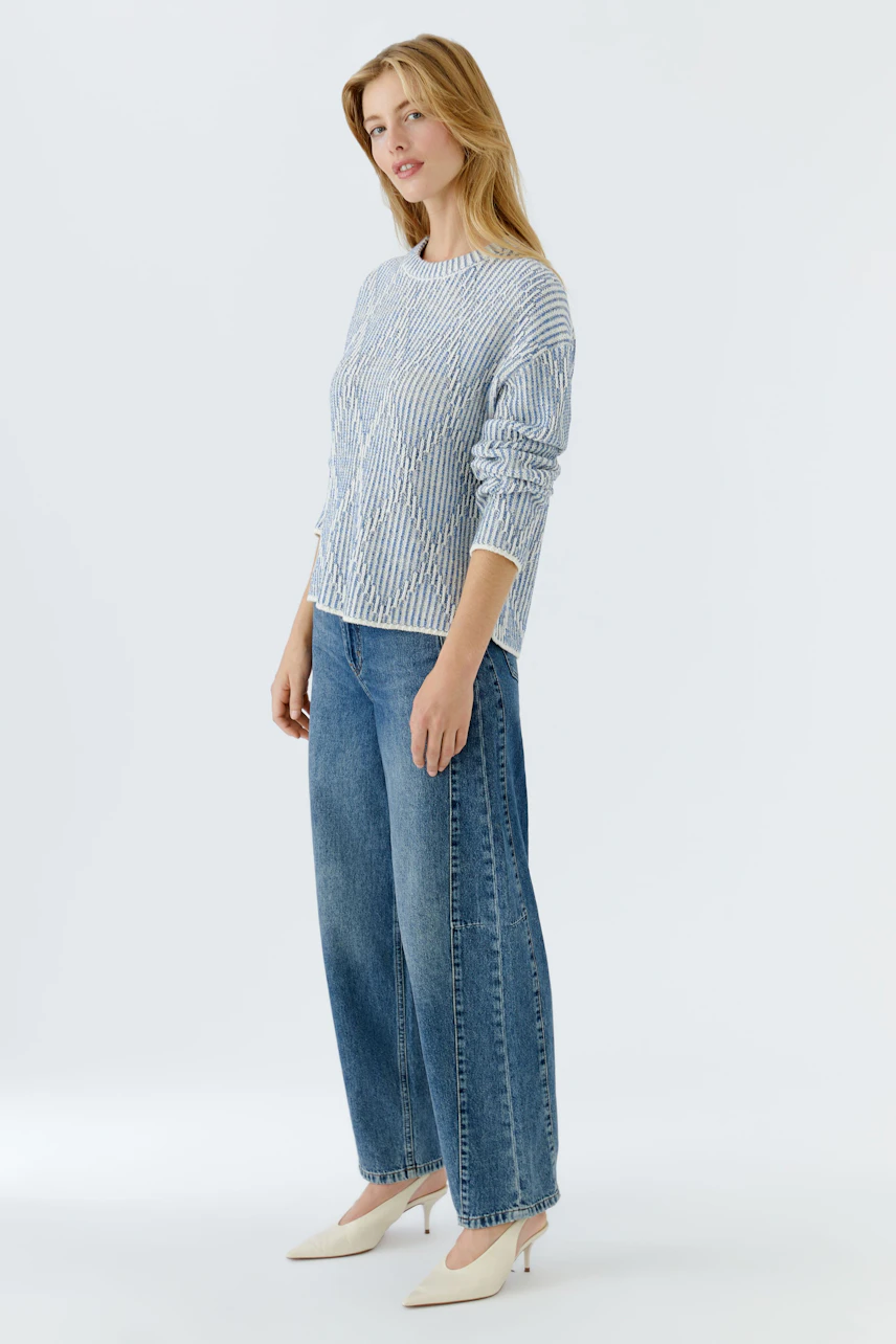 Casual women's pullover: Young woman in a striped pullover paired with wide jeans, standing confidently.