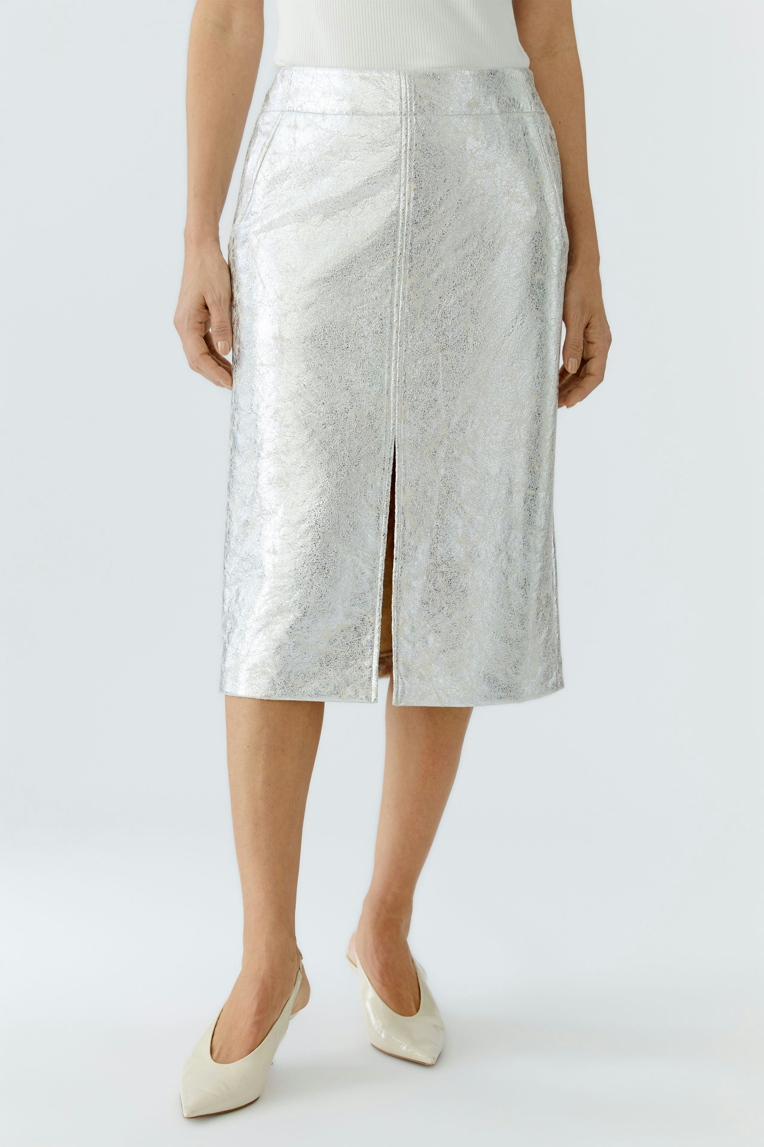 Shiny pencil skirt: Woman in a silver pencil skirt with a front slit, paired with light-colored heels.