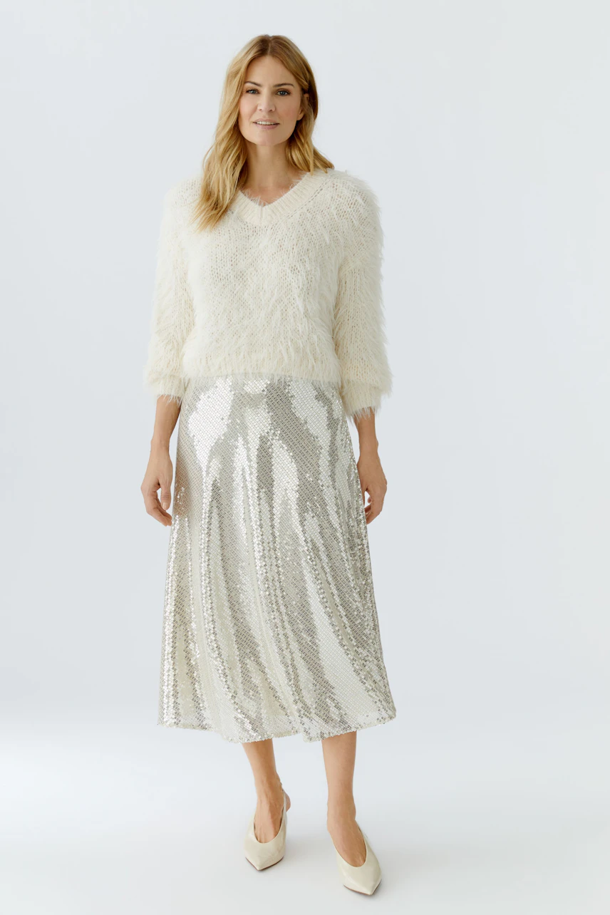 A-line skirt: Woman in a fluffy white pullover and a shiny silver A-line skirt, posing confidently.