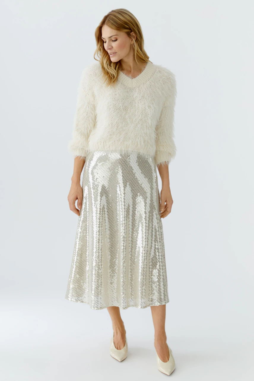 A-line skirt: Woman in a shimmering silver A-line skirt paired with a cozy white pullover.