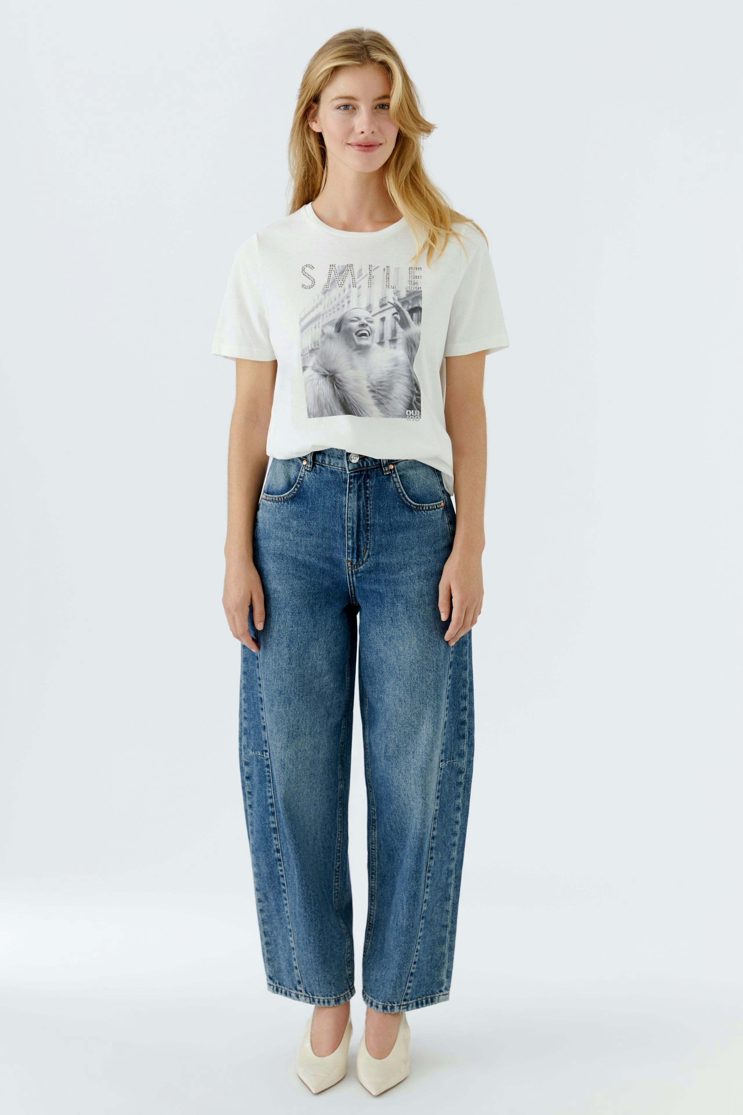 Casual women's T-shirt: Young woman in a white tee with a graphic print and relaxed fit jeans.