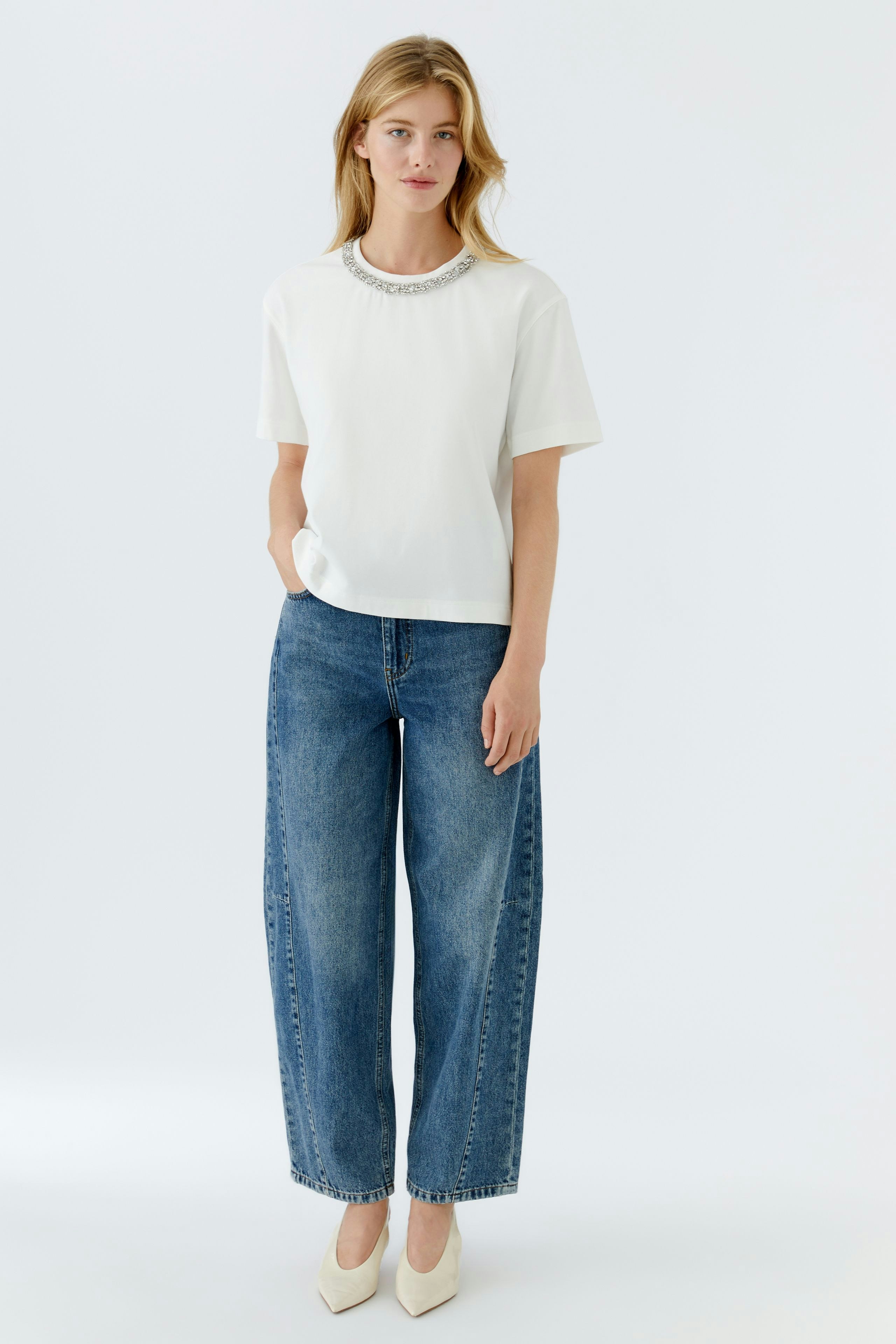 Casual women's T-shirt: Young woman in a white T-shirt with a decorative neckline and wide jeans.