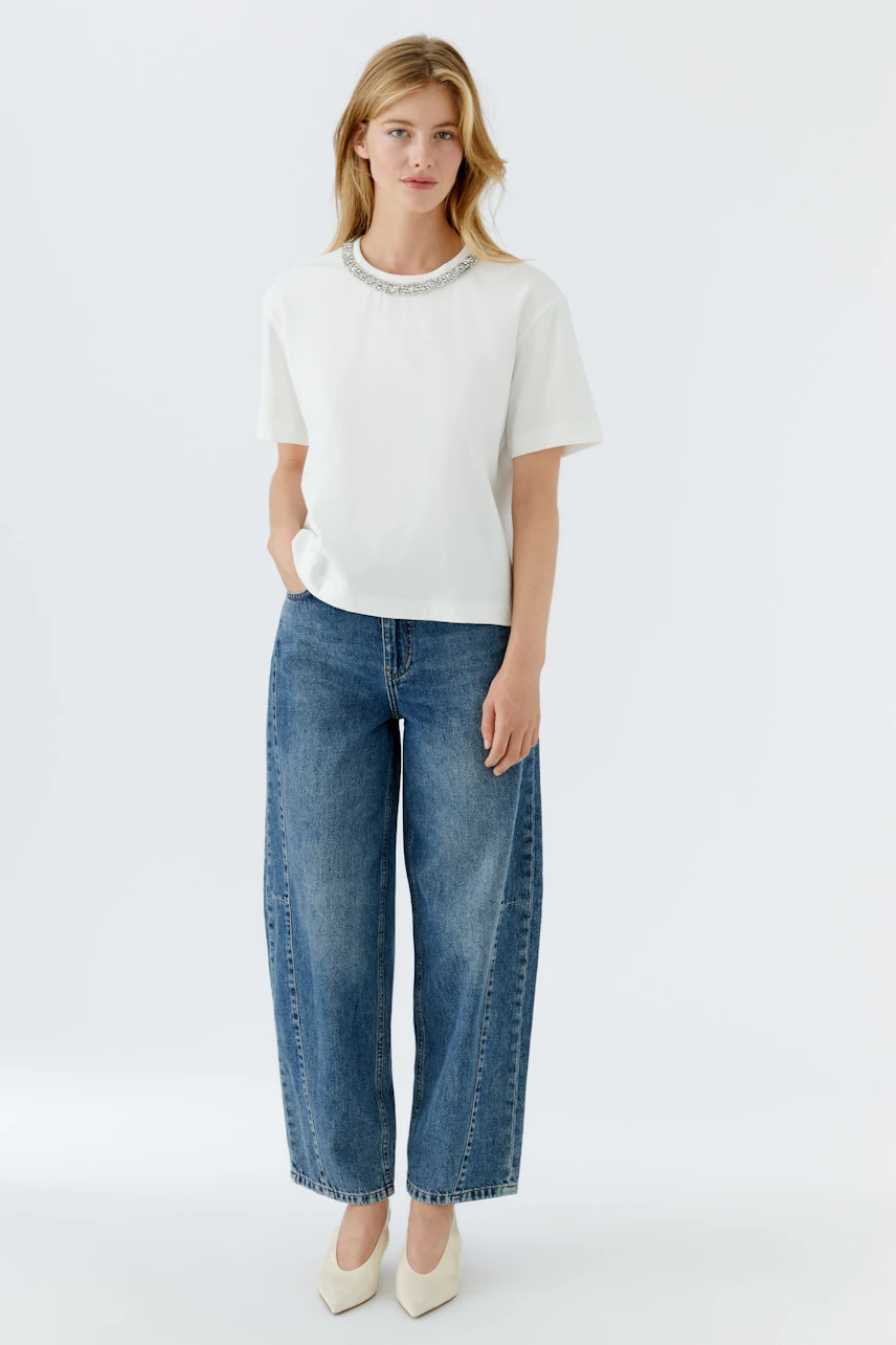Casual women's T-shirt: Young woman in a white T-shirt with a decorative neckline and wide jeans.