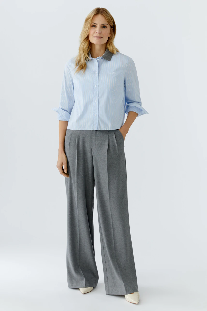 Casual women's blouse: Woman in a light blue button-up shirt paired with wide gray trousers.