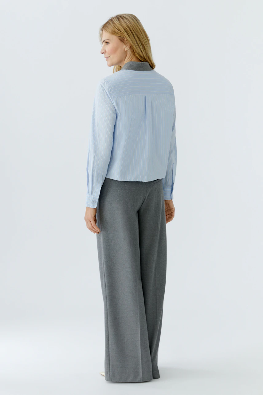 Casual women's blouse: Woman in a light blue striped blouse with a relaxed fit and back detail.