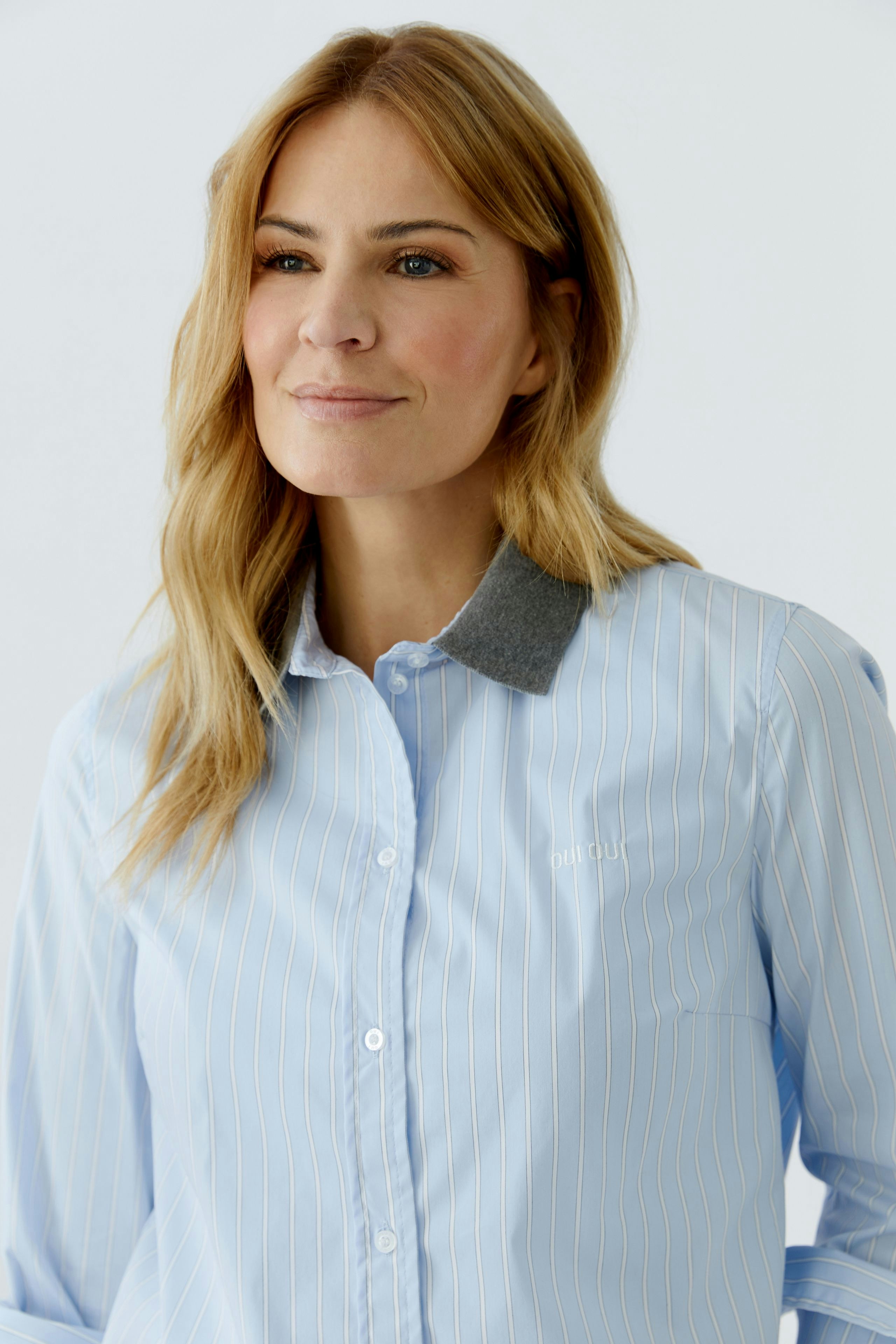 Casual women's blouse: Woman in a light blue striped blouse with a grey collar, smiling confidently.