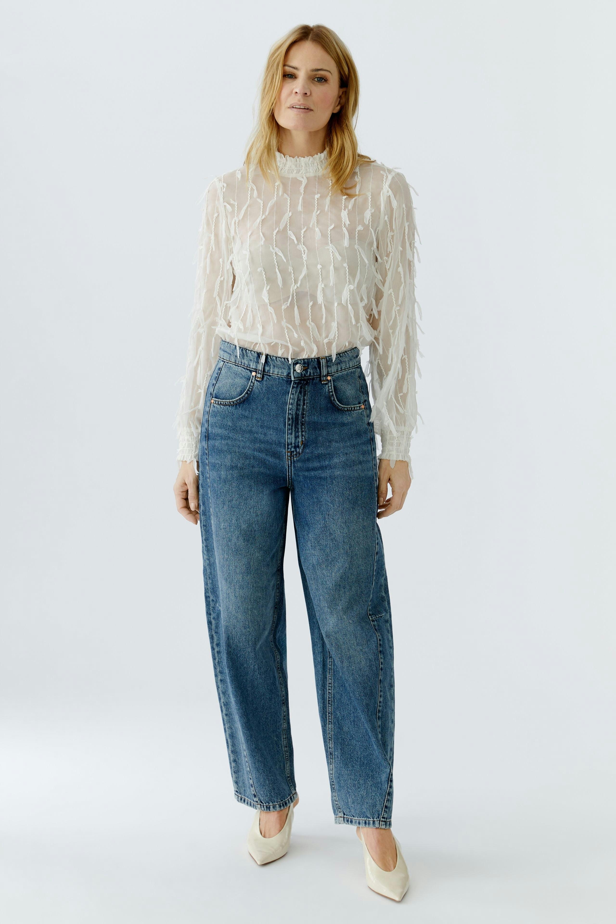 Light blouse: Woman in a sheer, textured blouse paired with high-waisted jeans.