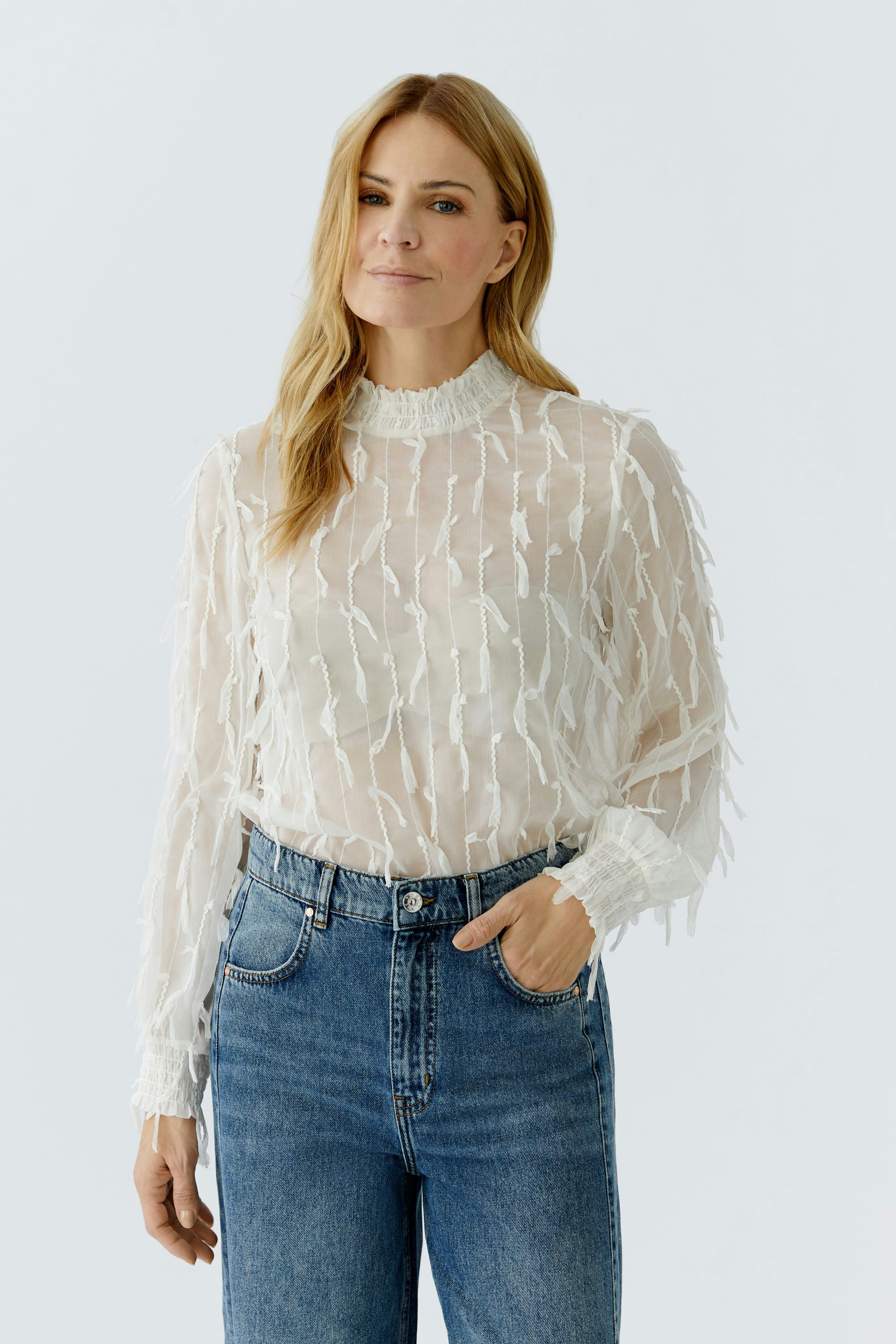 Lightweight blouse: Woman in a sheer, textured blouse paired with high-waisted jeans.