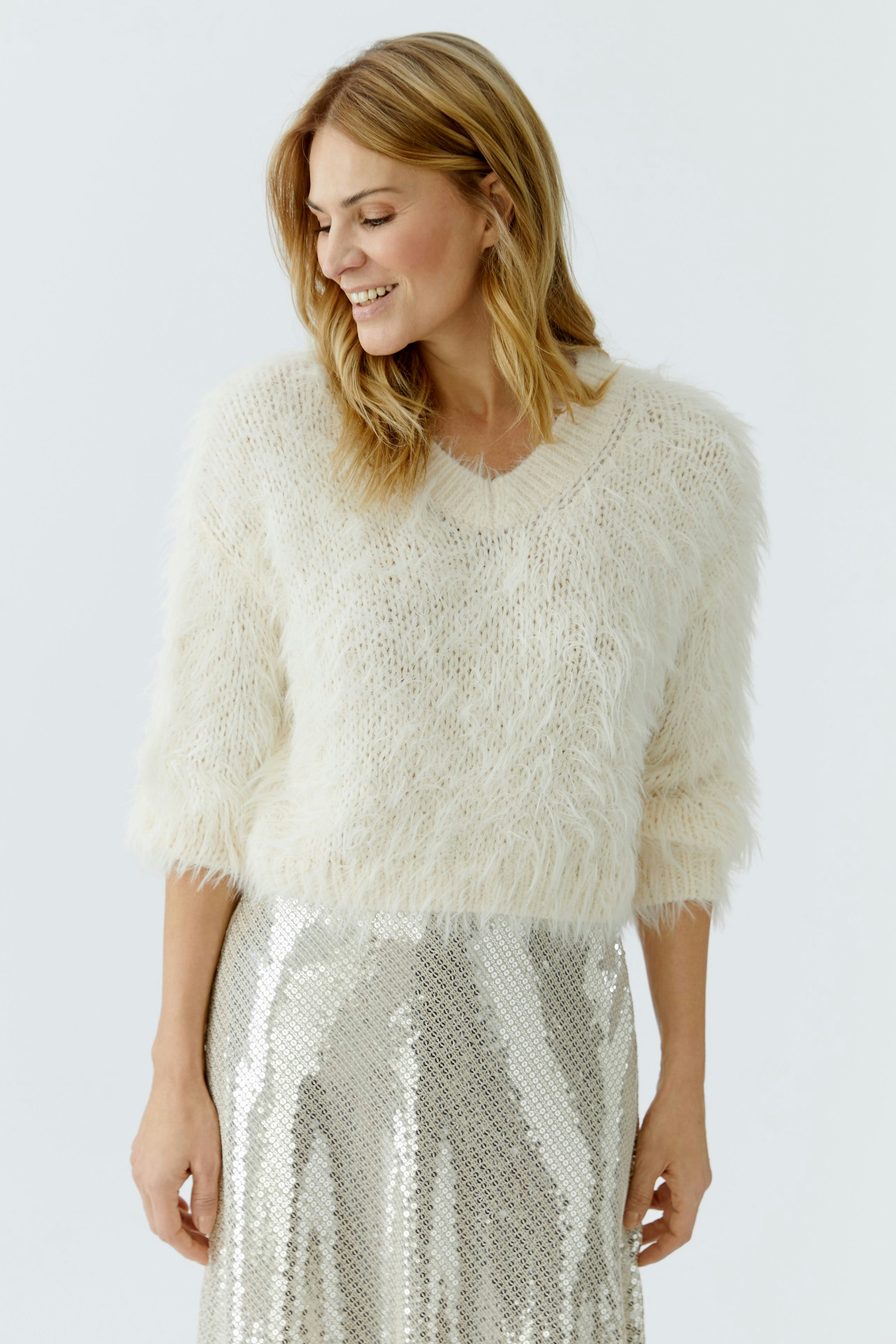 Cozy women's pullover: A woman in a fluffy cream pullover smiles, paired with a shiny silver skirt.