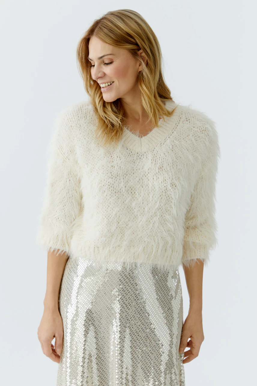 Cozy women's pullover: A woman in a fluffy cream pullover smiles, paired with a shiny silver skirt.