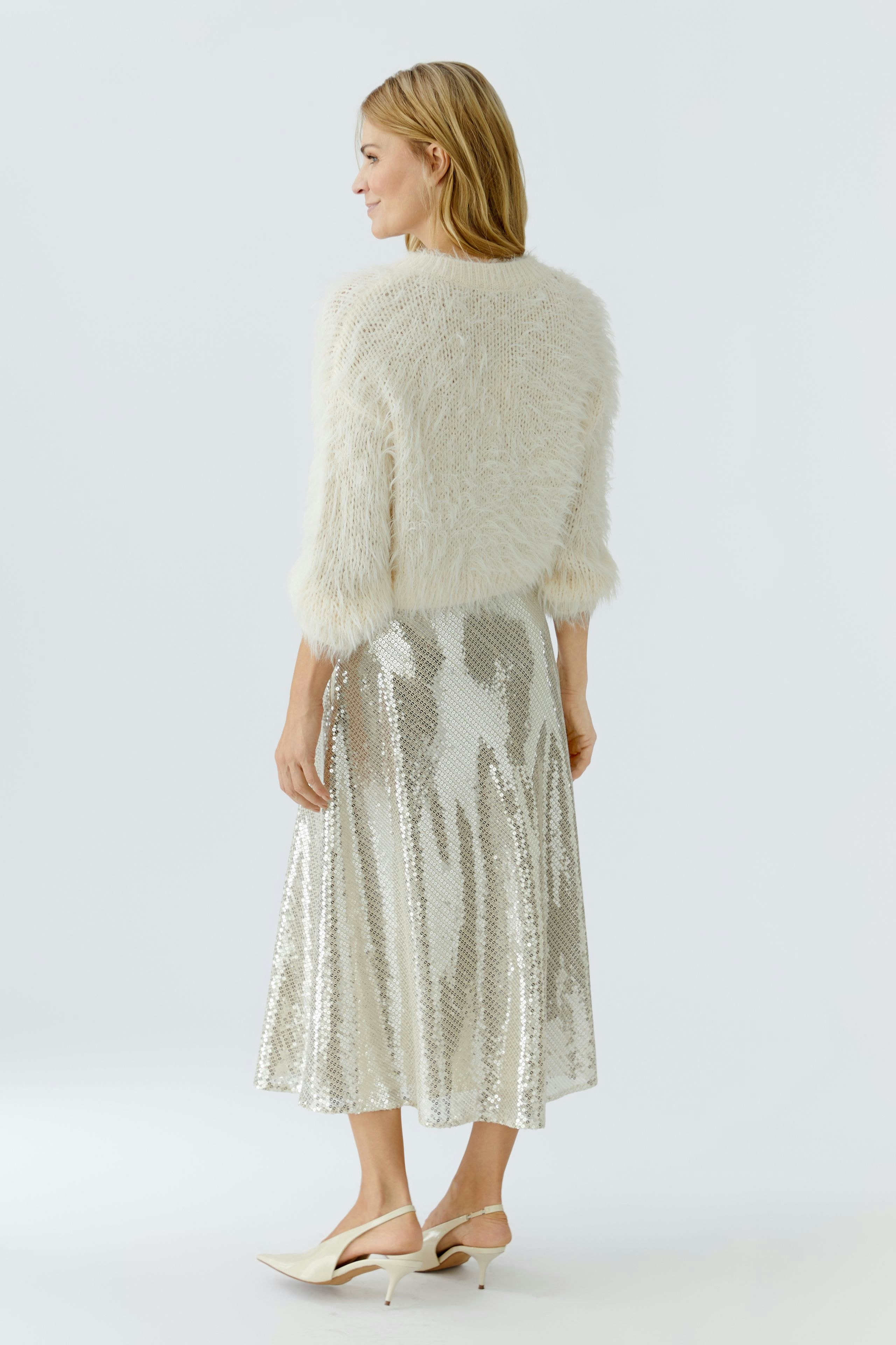 Cozy women's pullover: A woman in a fluffy white pullover paired with a shiny silver skirt.
