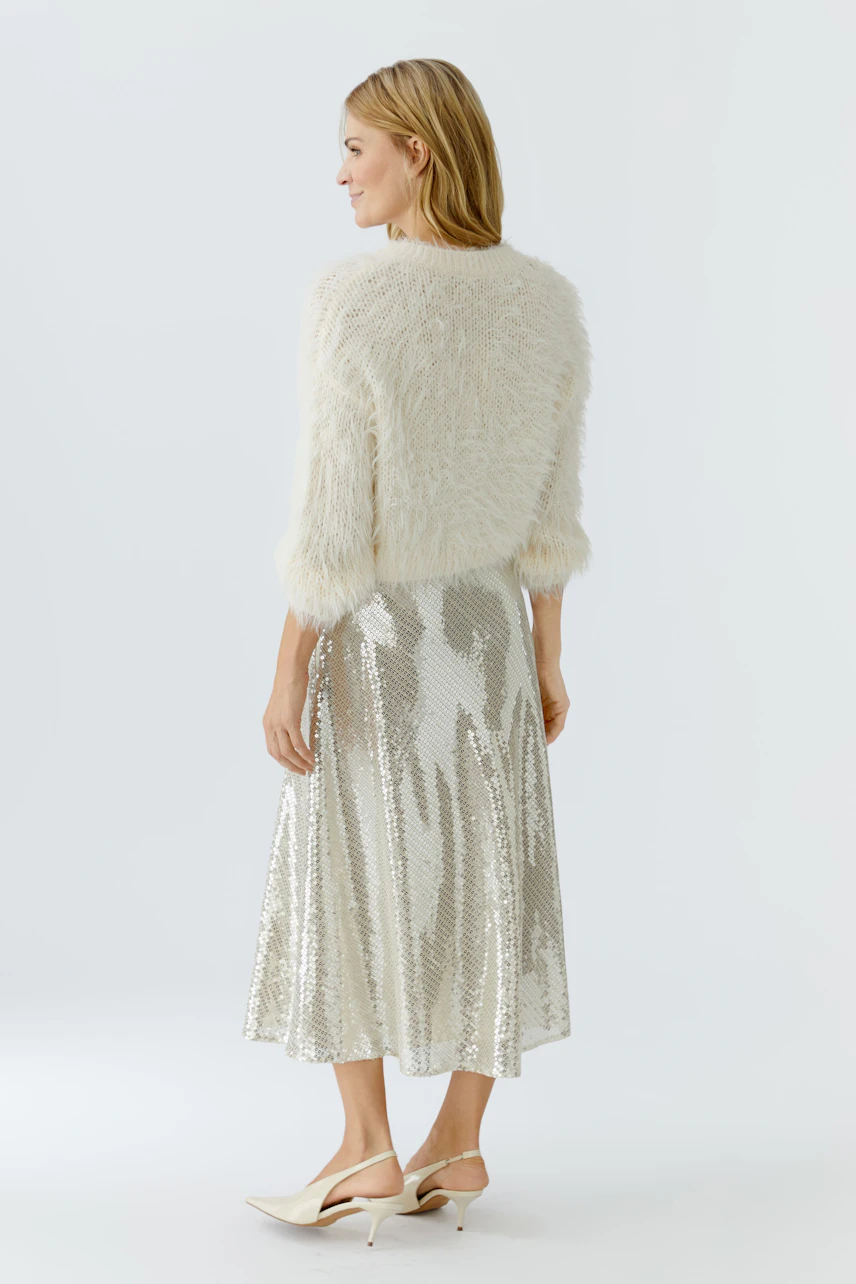 Cozy women's pullover: A woman in a fluffy white pullover paired with a shiny silver skirt.