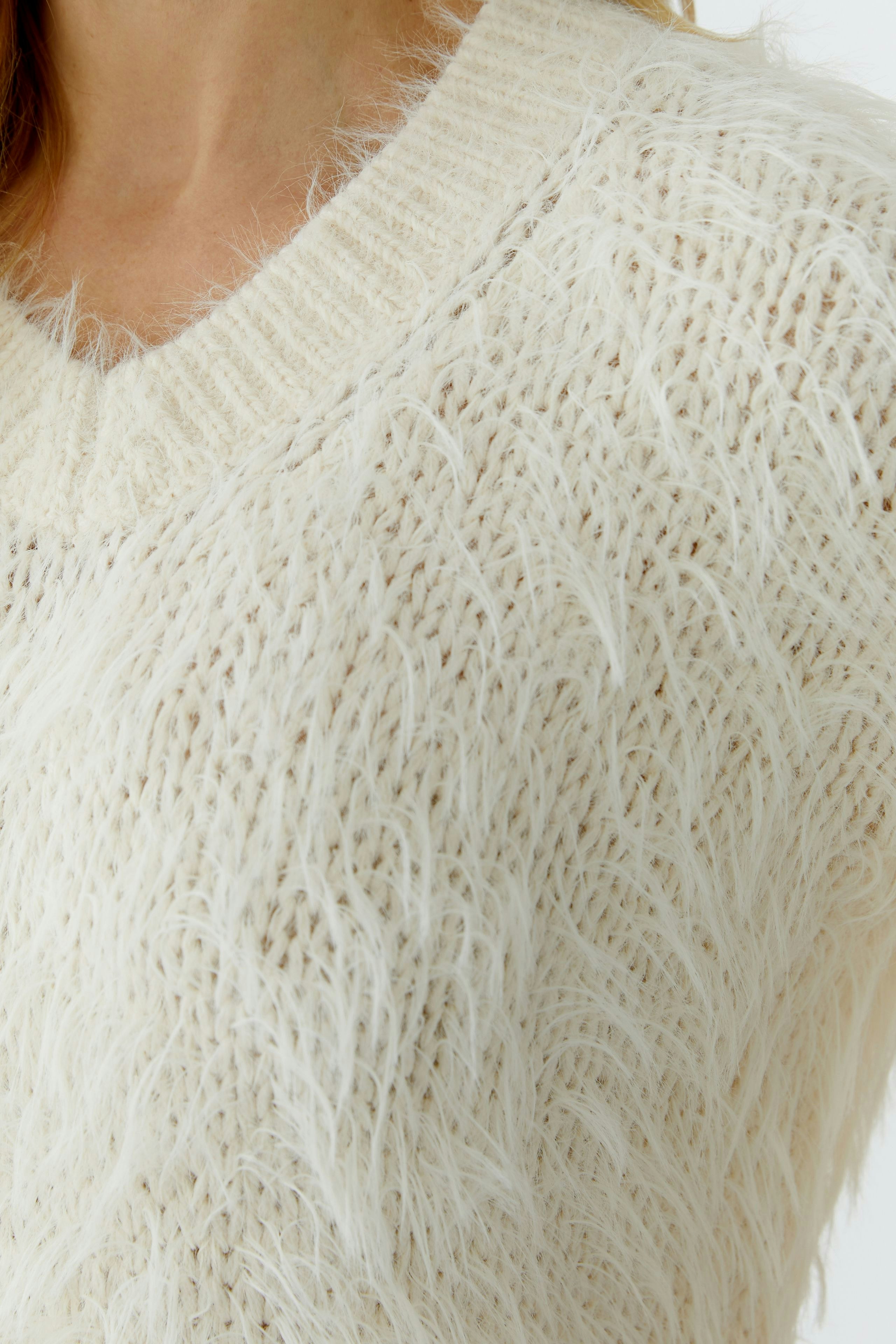 Cozy women's pullover: Close-up of a woman in a fluffy cream pullover with a V-neck.