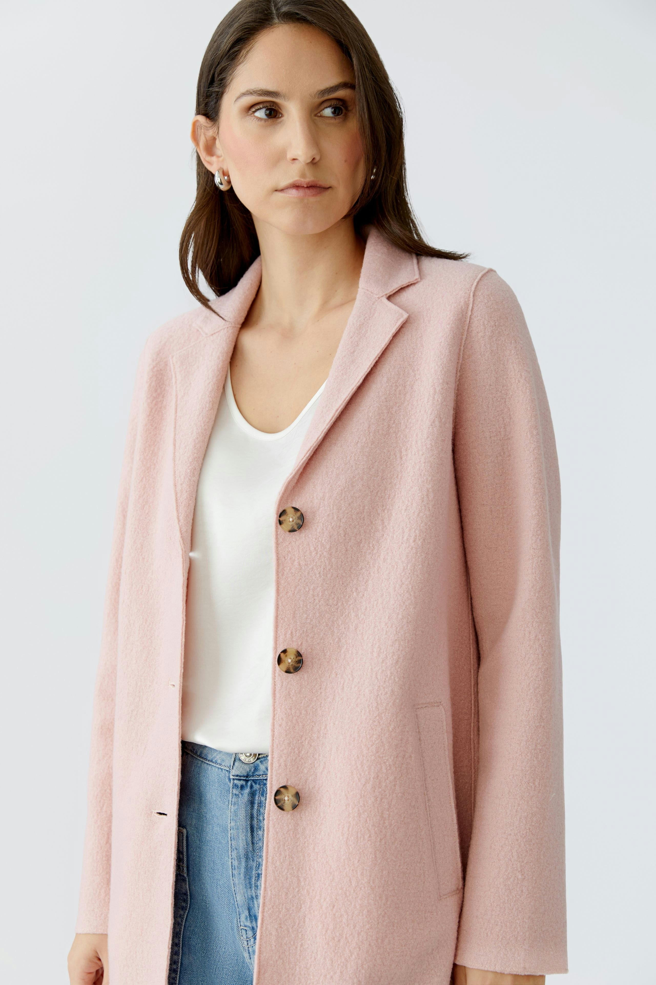 Damen Wollmantel: Frau in rosa Mantel mit Knöpfen und lässigem Shirt, kombiniert mit Jeans.