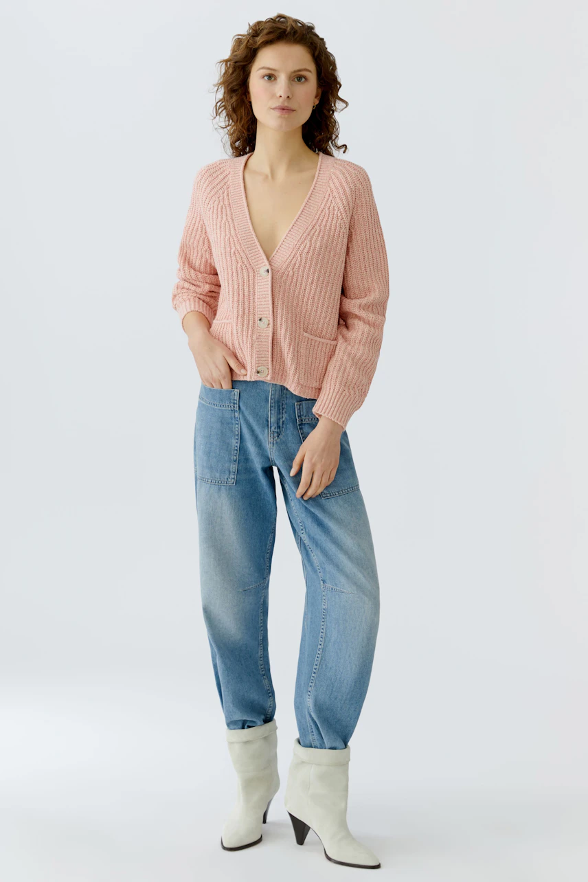 Casual women's cardigan: A woman in a pink knitted cardigan with buttons and relaxed jeans.