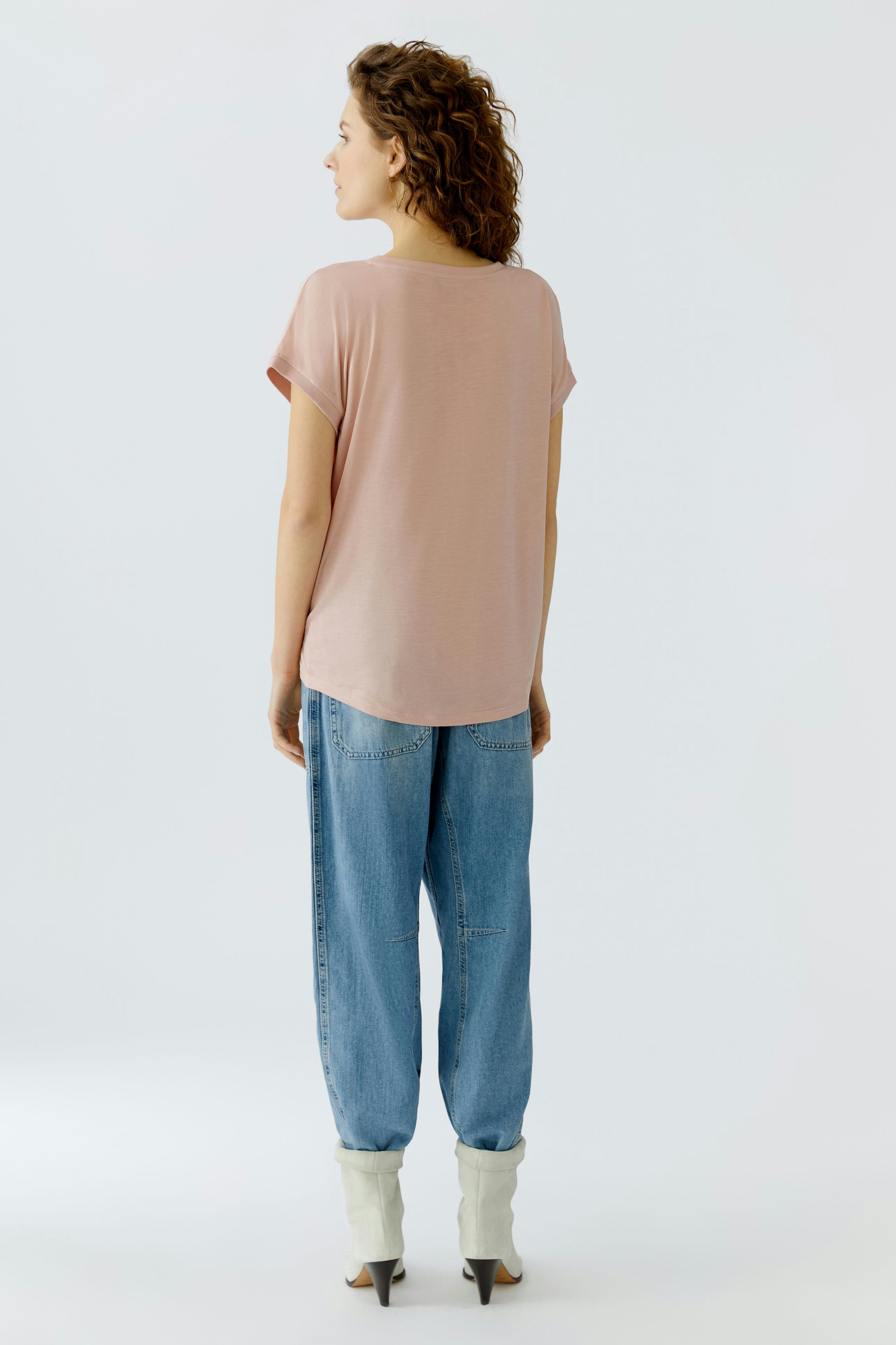 Casual women's blouse shirt: Woman in a light pink top with rolled sleeves and relaxed fit jeans.