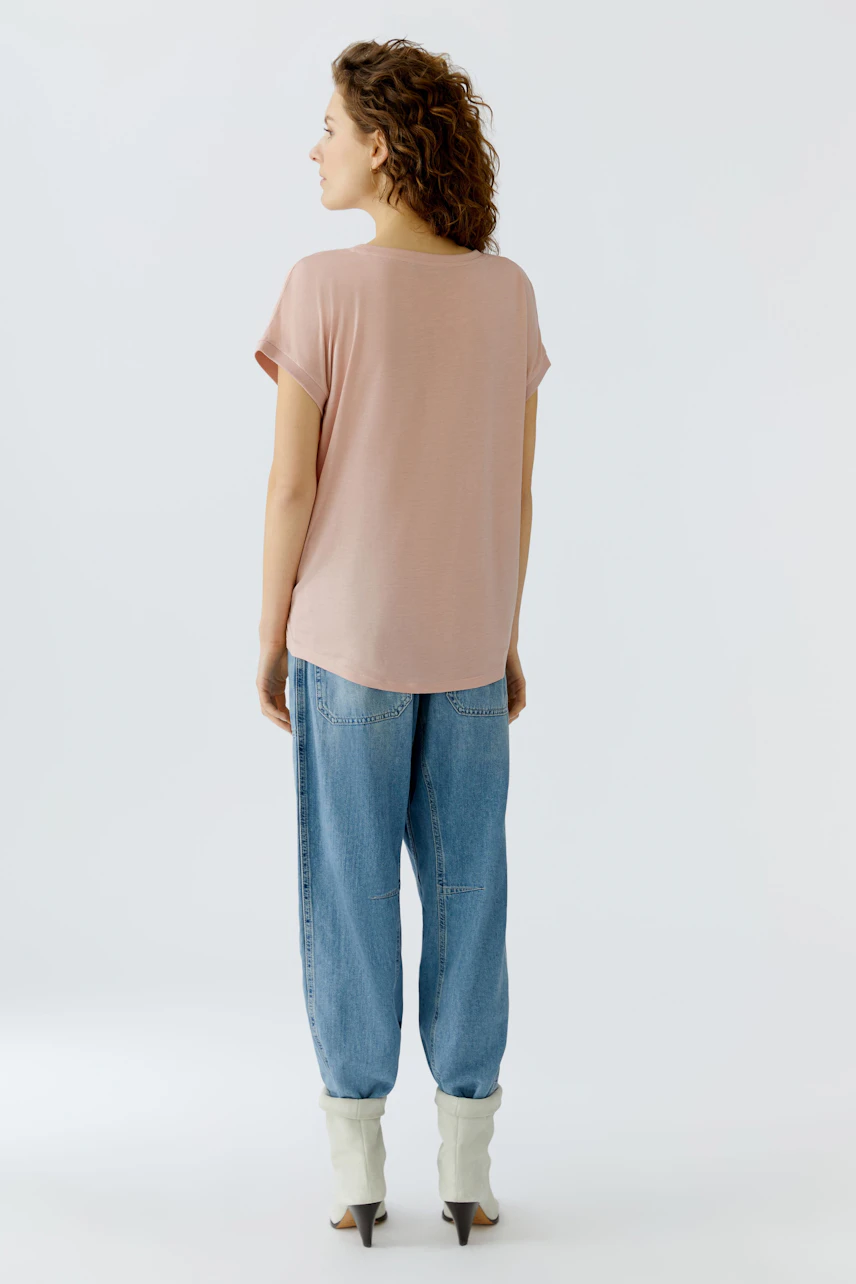 Casual women's blouse shirt: Woman in a light pink top with rolled sleeves and relaxed fit jeans.