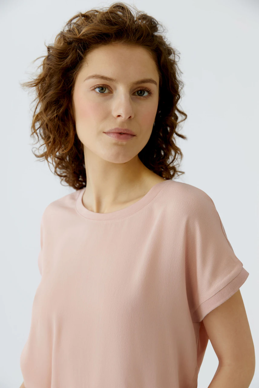 Casual women's blouse shirt: Woman in a soft pink top with rolled sleeves, looking confidently at the camera.