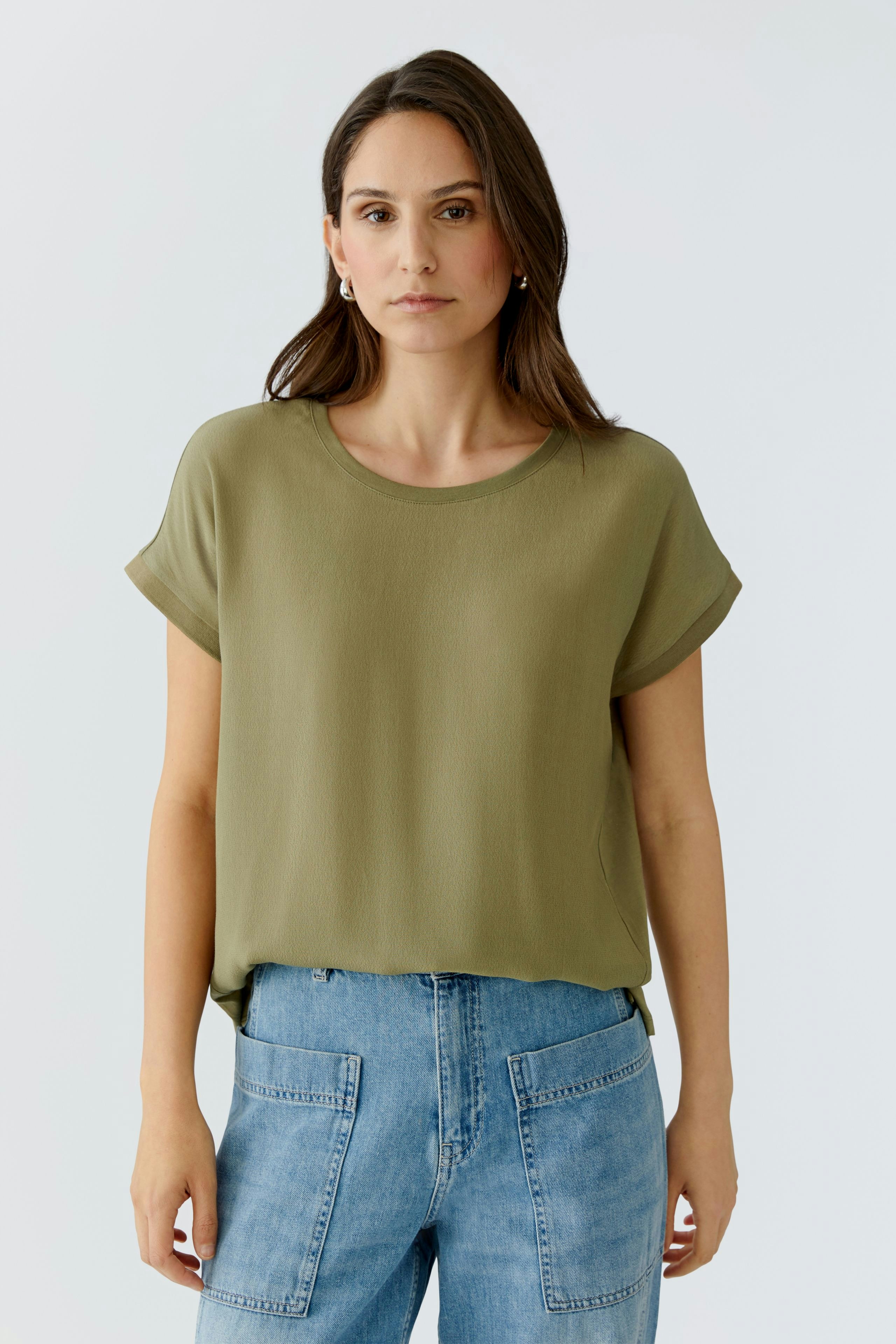 Casual women's blouse shirt: Woman in a relaxed olive green top paired with light blue jeans.