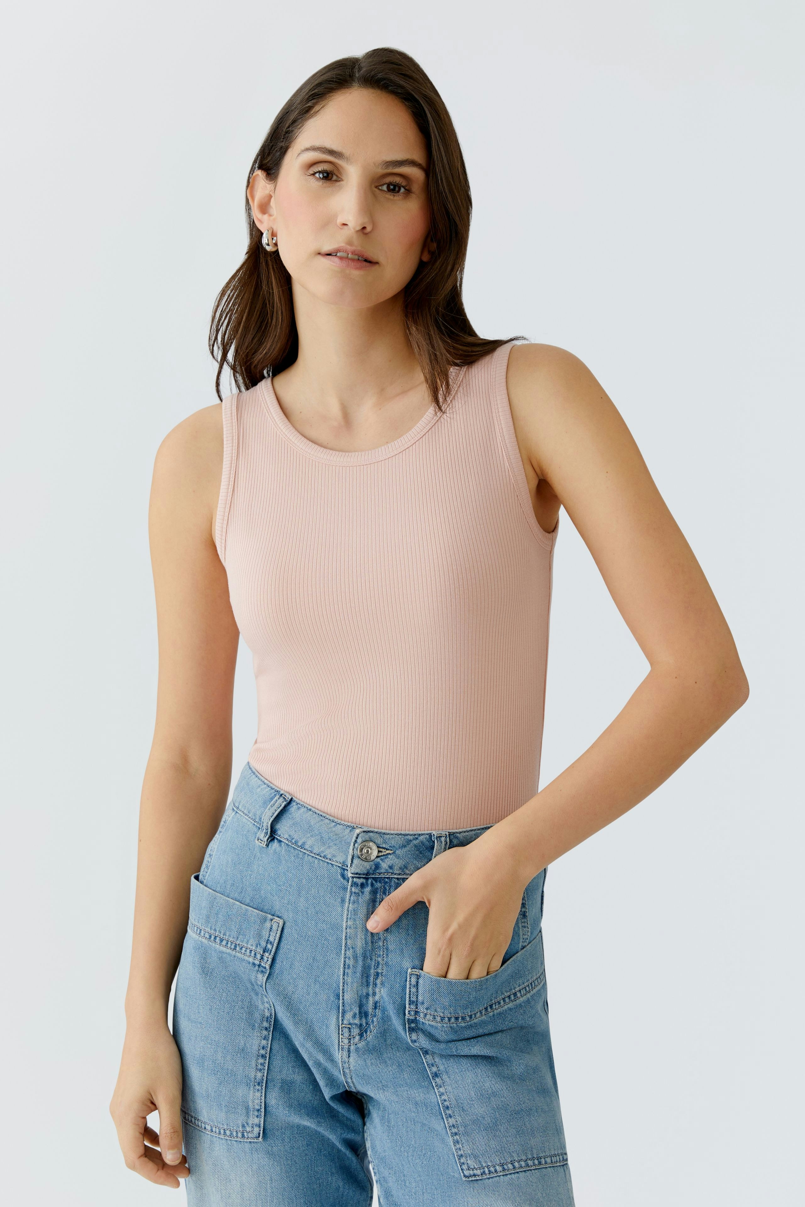Casual women's top: A woman in a light pink ribbed tank top paired with denim shorts.