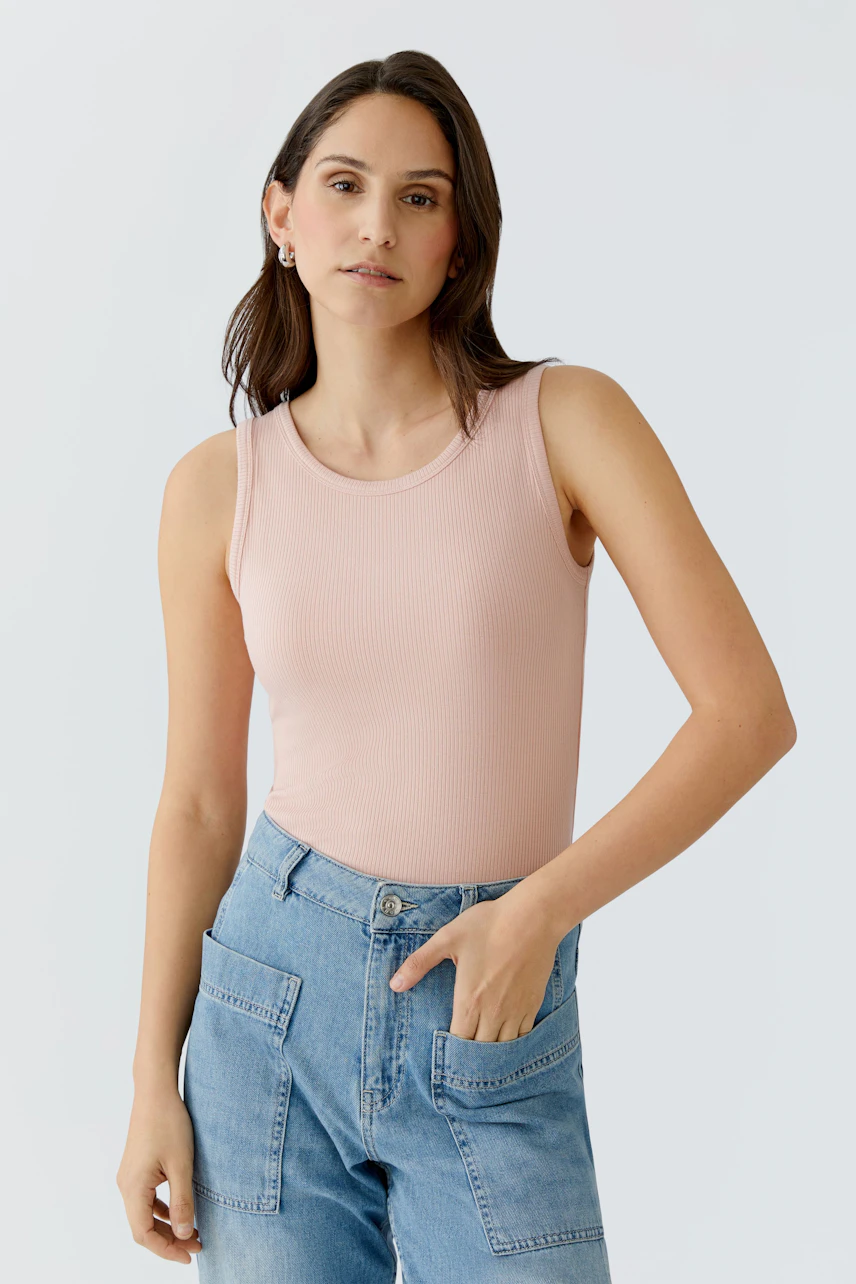 Casual women's top: A woman in a light pink ribbed tank top paired with denim shorts.