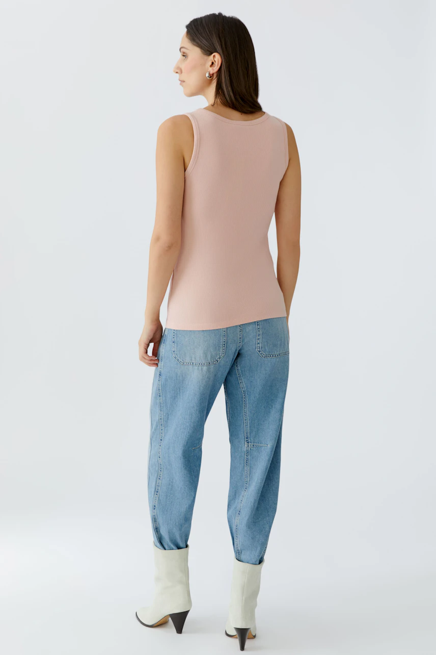 Casual women's top: Young woman in a light pink sleeveless top paired with relaxed jeans.