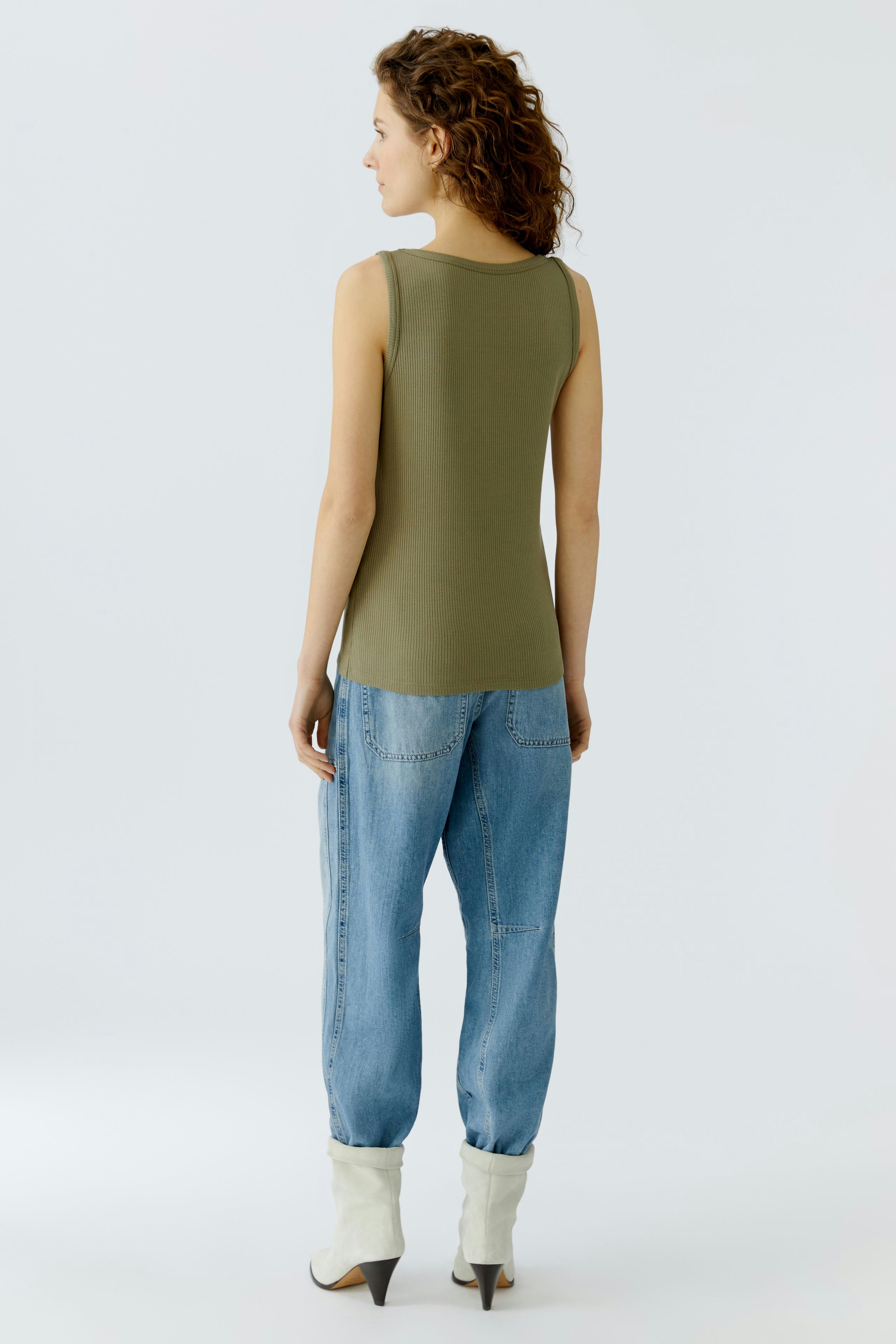 Casual women's top: A woman in a fitted olive green tank top paired with relaxed denim pants.