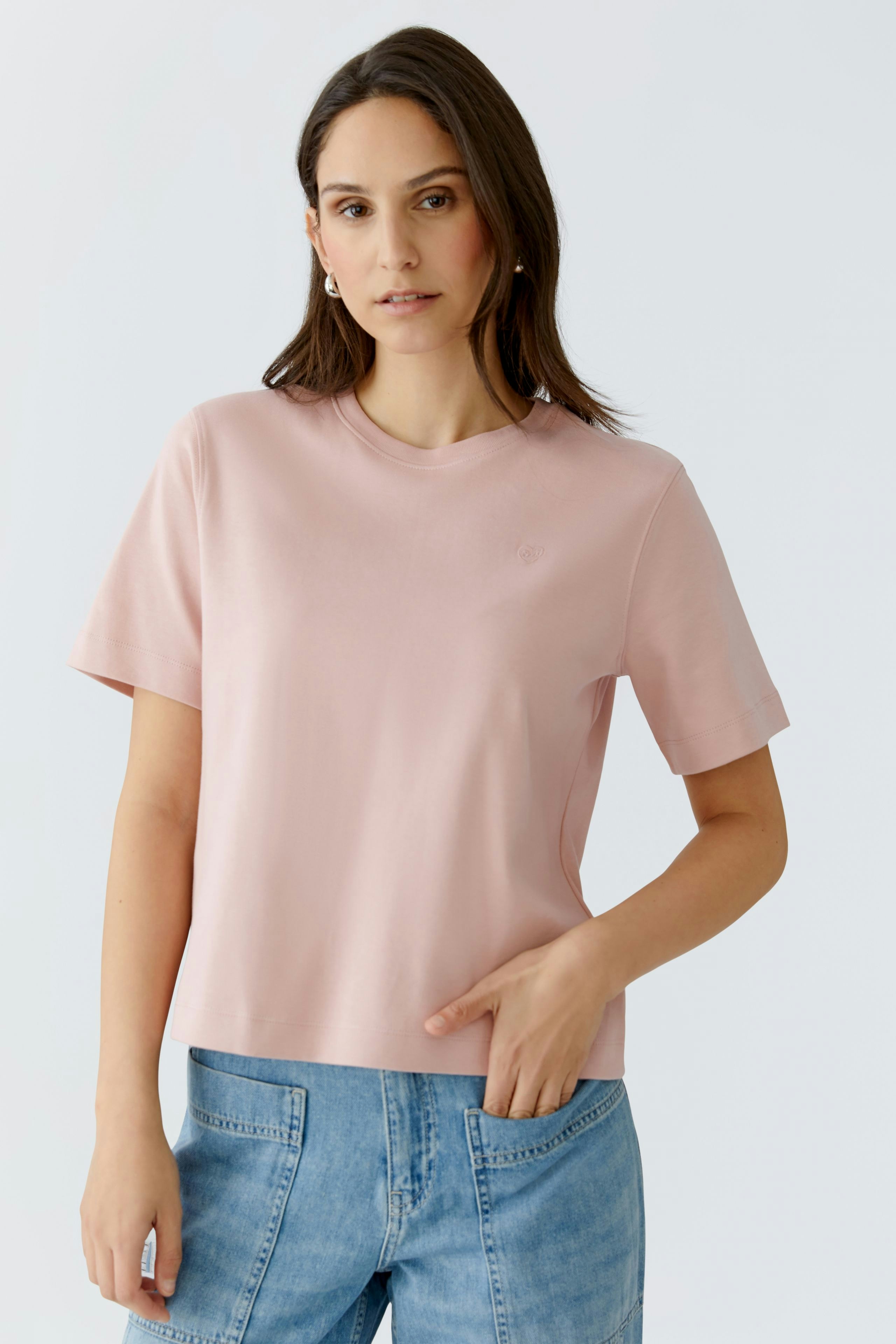 Casual women's T-shirt: Young woman in a light pink tee with short sleeves and relaxed fit.