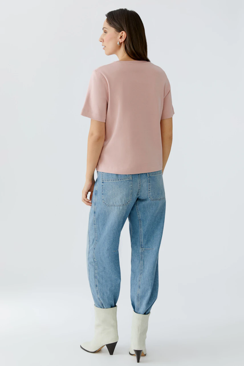 Damen-T-Shirt in zartem Rosa: Frau trägt lässiges Shirt mit kurzen Ärmeln und bequemen Jeans.