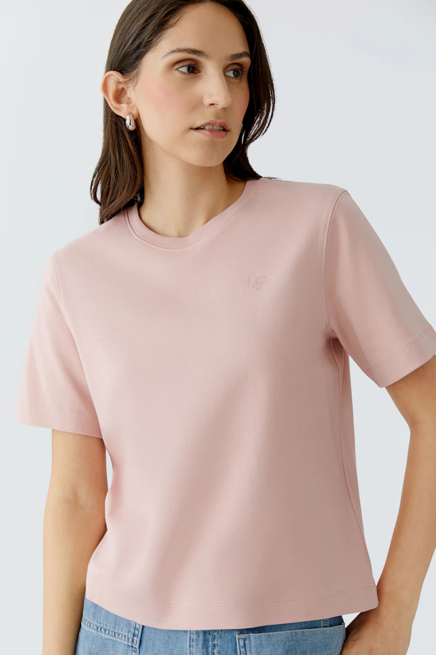 Damen-T-Shirt in zartem Rosa: Frau trägt ein schlichtes, lässiges T-Shirt mit kurzen Ärmeln.