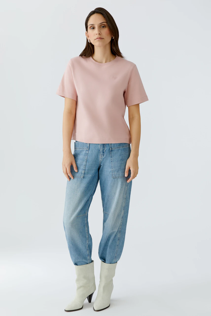 Bequemes Damen-T-Shirt: Frau trägt ein rosa T-Shirt mit lässigen Jeans und modischen Stiefeln.