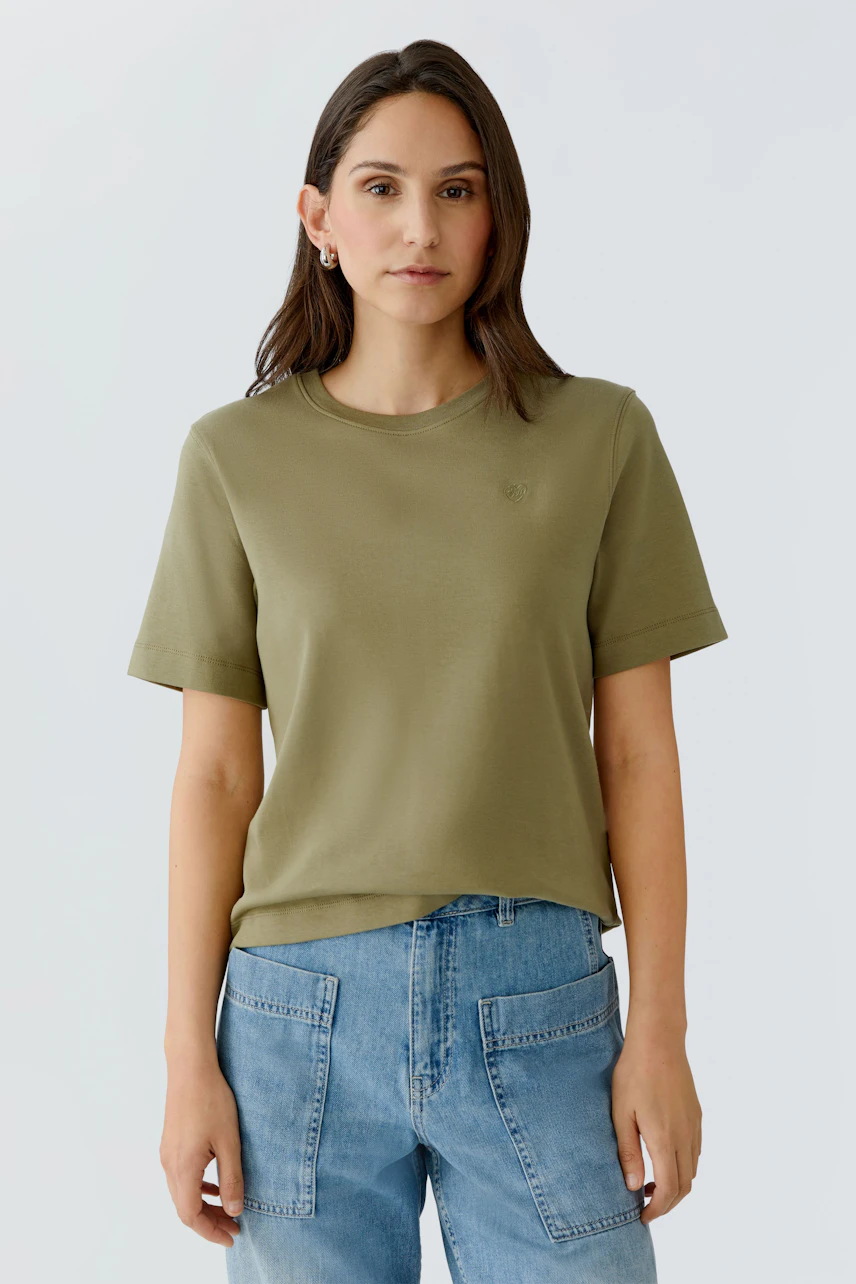 Bequeme Damen-T-Shirt: Frau trägt ein olivgrünes T-Shirt mit kurzen Ärmeln und lässigen Jeans.