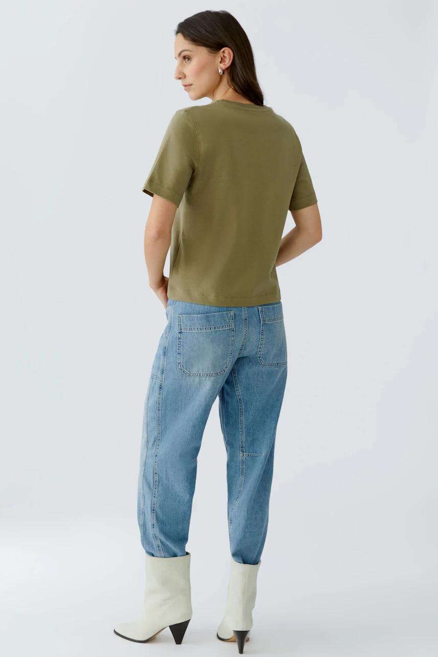 Bequemes Damen-T-Shirt: Frau in olivgrünem T-Shirt und lässigen Jeans von hinten.
