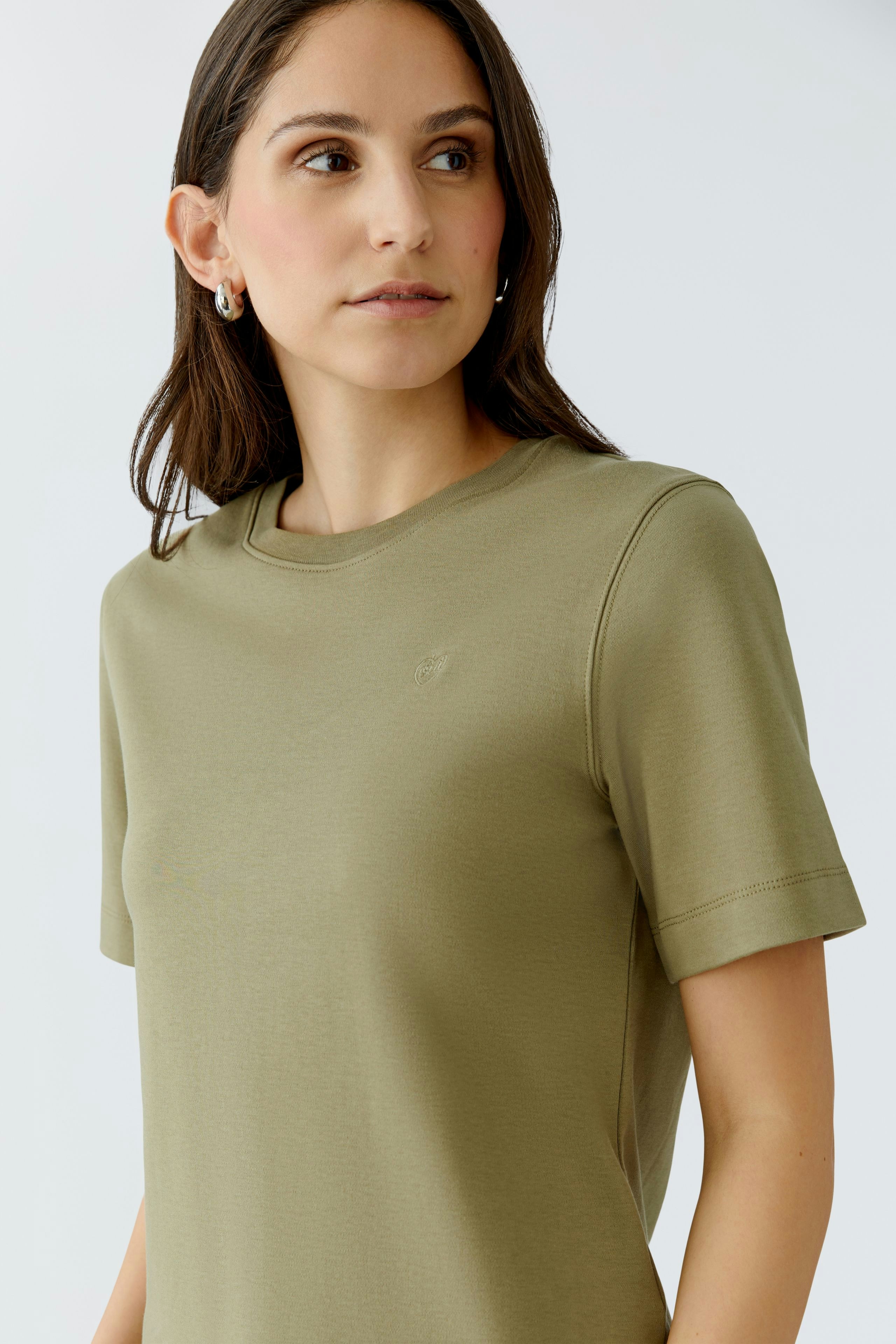 Casual women's T-shirt: Young woman in a soft olive green tee with short sleeves, looking relaxed.
