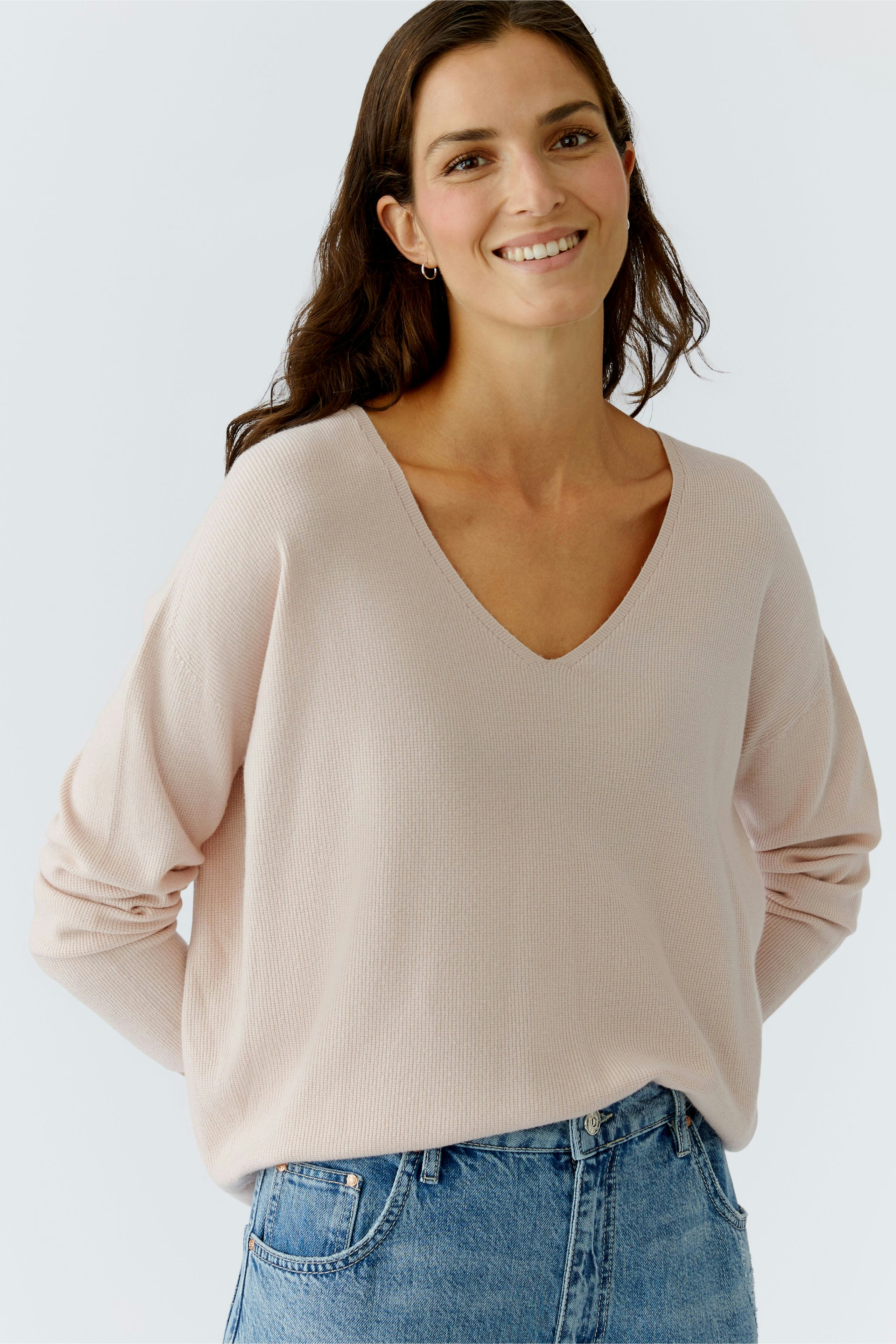 Casual women's pullover: Smiling woman in a light pink V-neck pullover paired with denim.