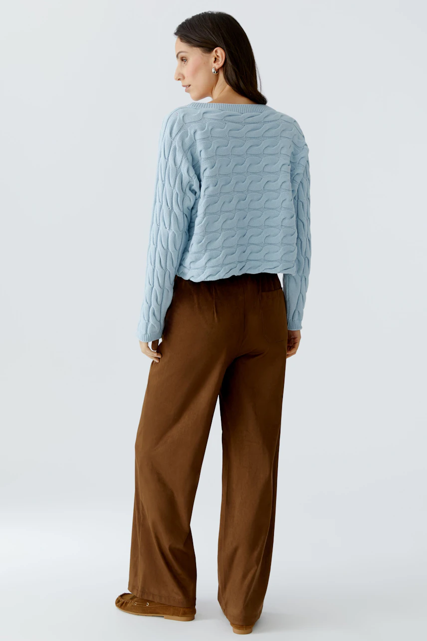 Damen-Pullover: Frau trägt einen hellblauen, strukturierten Pullover mit lässigem Schnitt und weiten Hosen.