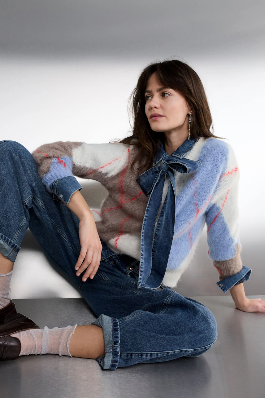 Casual women's pullover: Young woman in a colorful, patterned pullover with a bow detail, styled with denim.
