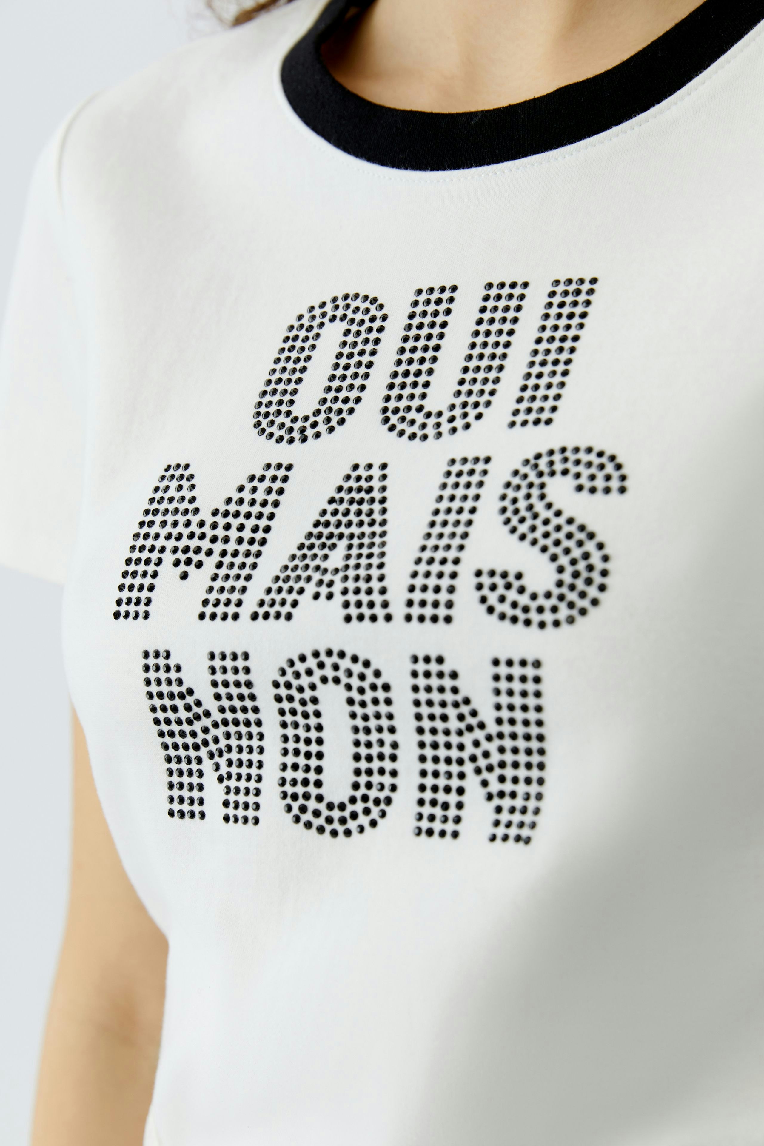 Damen-T-Shirt: Frau trägt ein weißes T-Shirt mit schwarzem Rundhalsausschnitt und glitzerndem Schriftzug.
