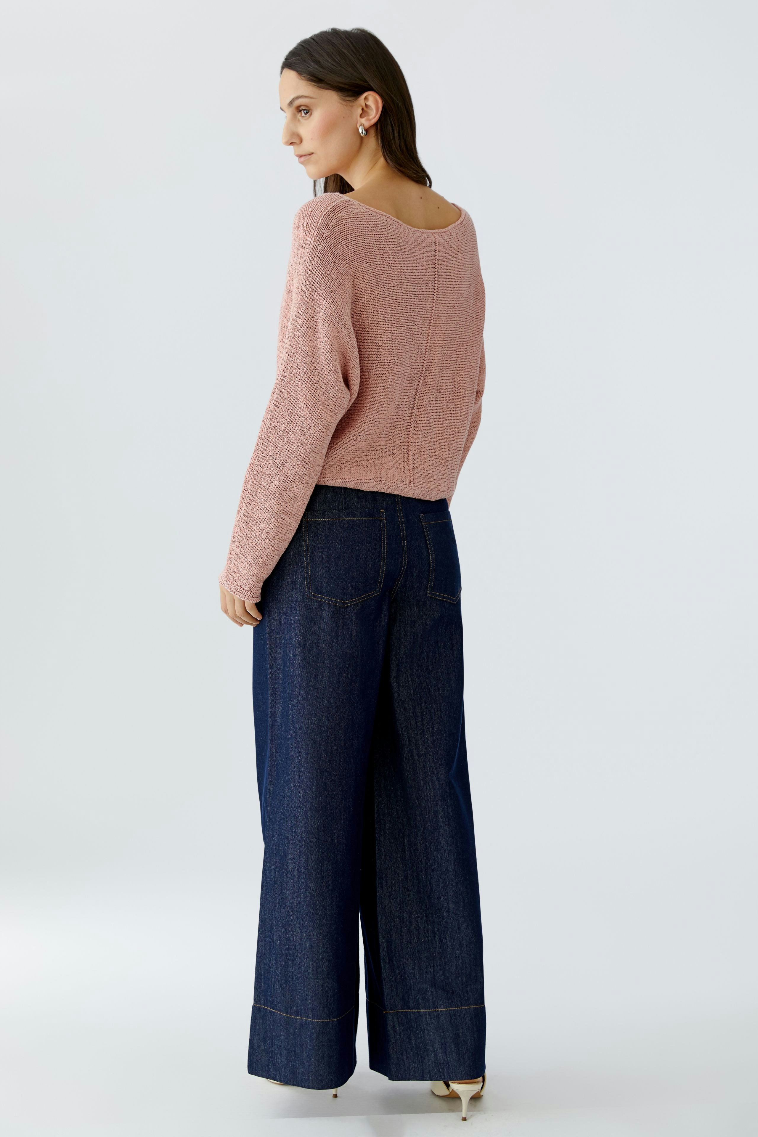 Damen-Pullover: Frau in rosafarbenem, lässigem Strickpullover mit weitem Schnitt und blauen Jeans.