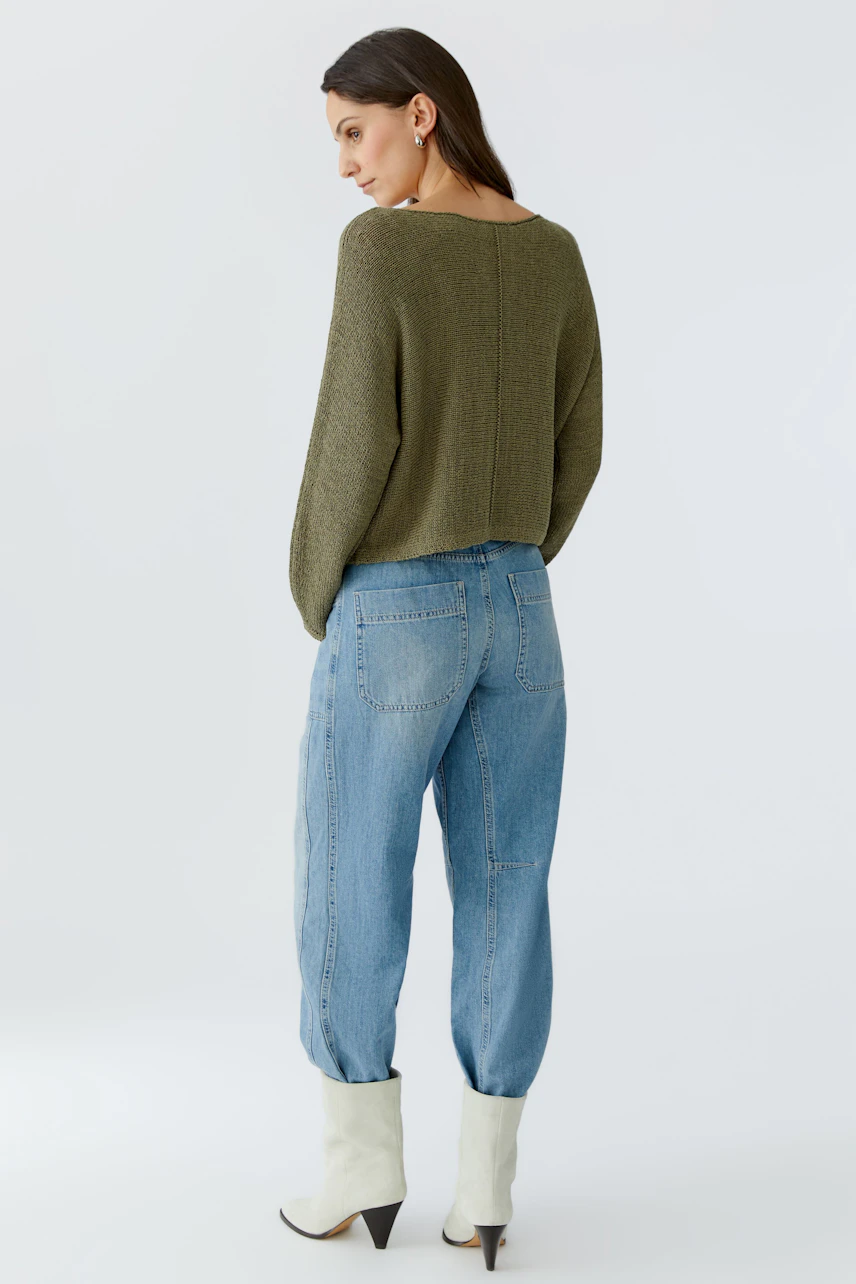 Casual women's pullover: A woman in a relaxed olive green pullover paired with light blue jeans.