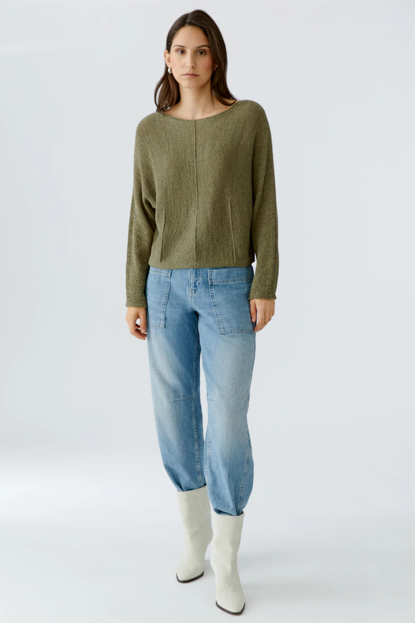 Casual women's pullover: A woman in a relaxed olive green pullover paired with light blue jeans.