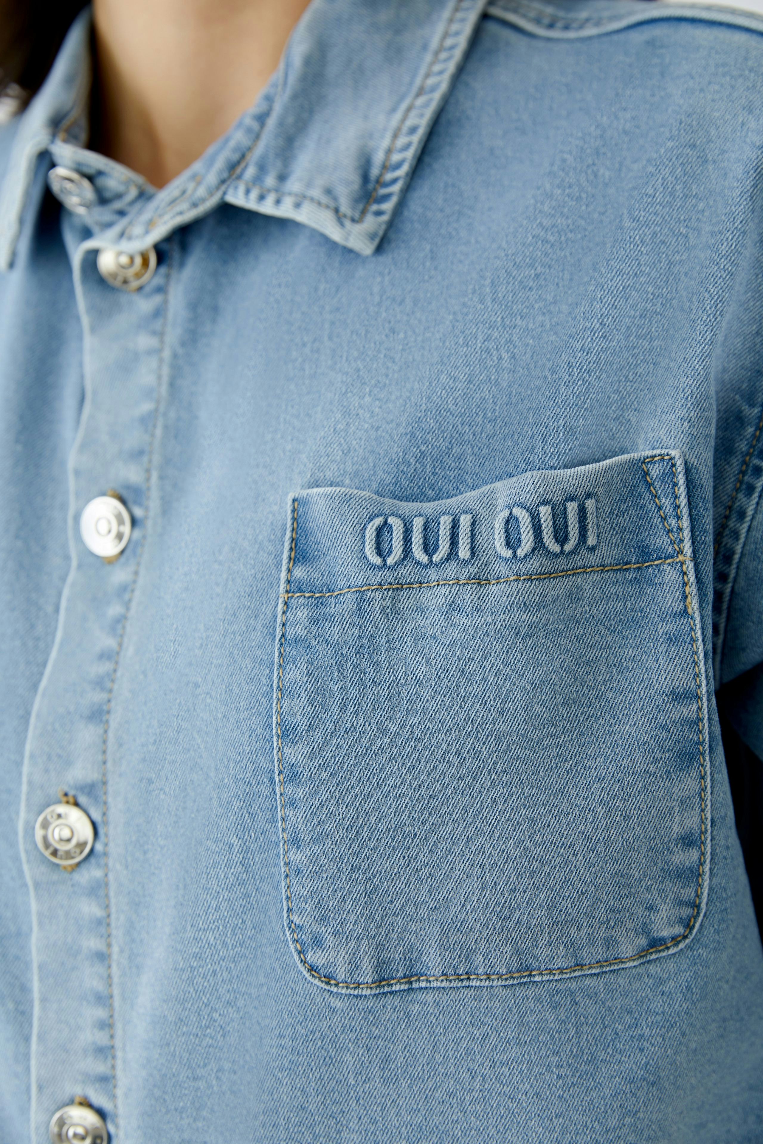 Casual women's blouse: Close-up of a woman in a light blue denim blouse with a pocket and logo.