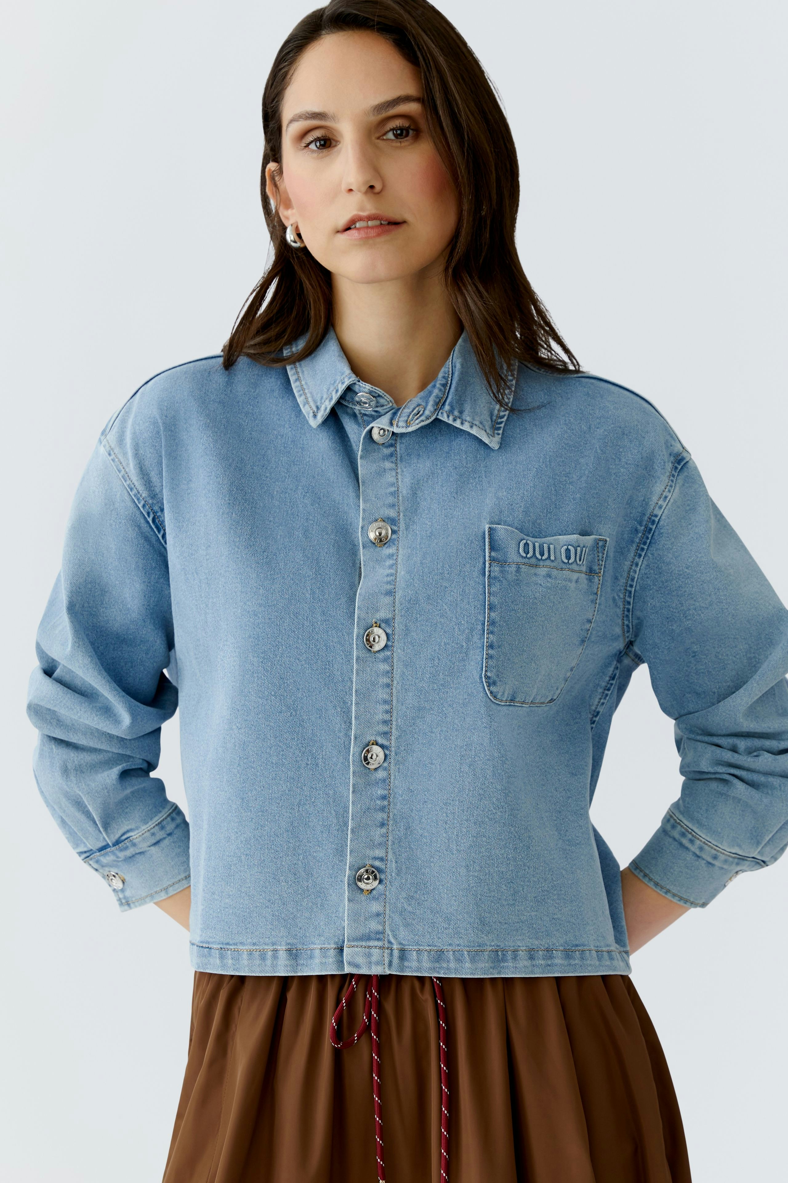 Casual women's blouse: A woman in a light blue denim blouse with a pocket, styled with a brown skirt.