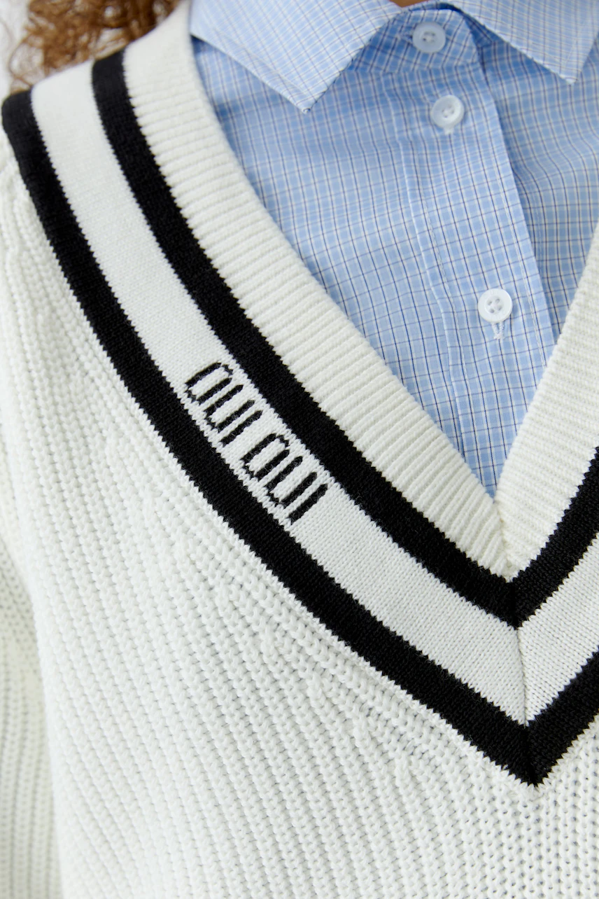 Casual women's pullover: Close-up of a white pullover with a V-neck and black stripes, worn over a shirt.