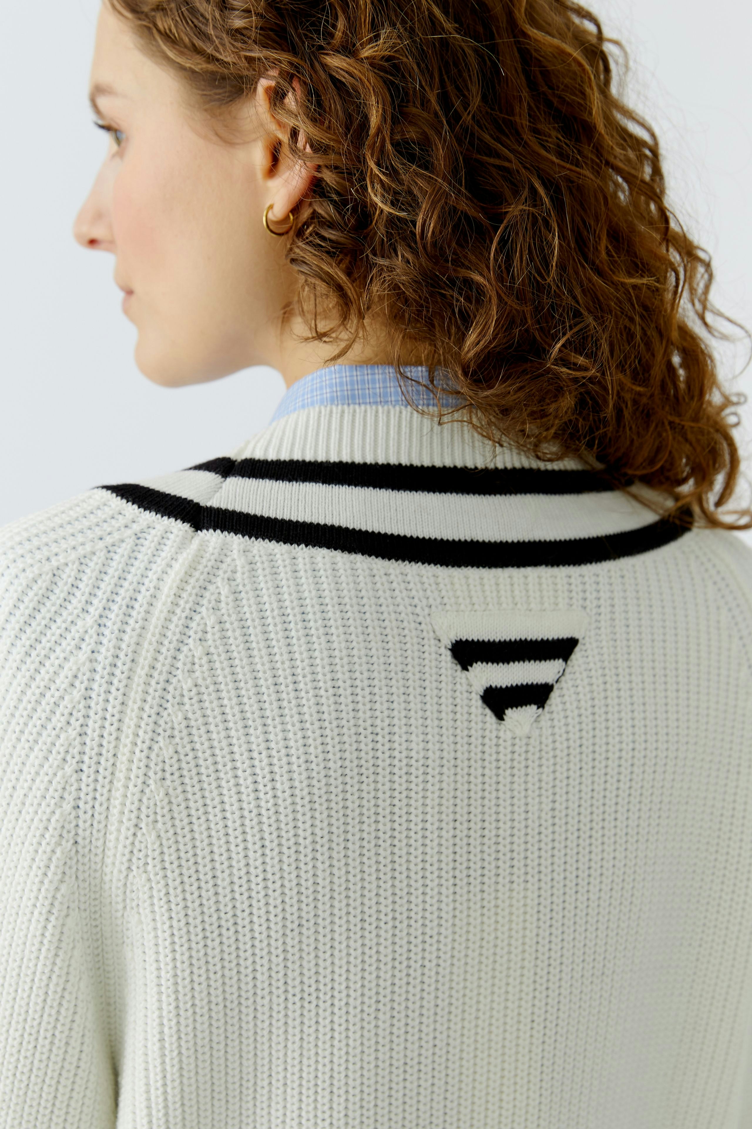 Casual women's pullover: A woman with curly hair wears a white knitted pullover with black stripes.