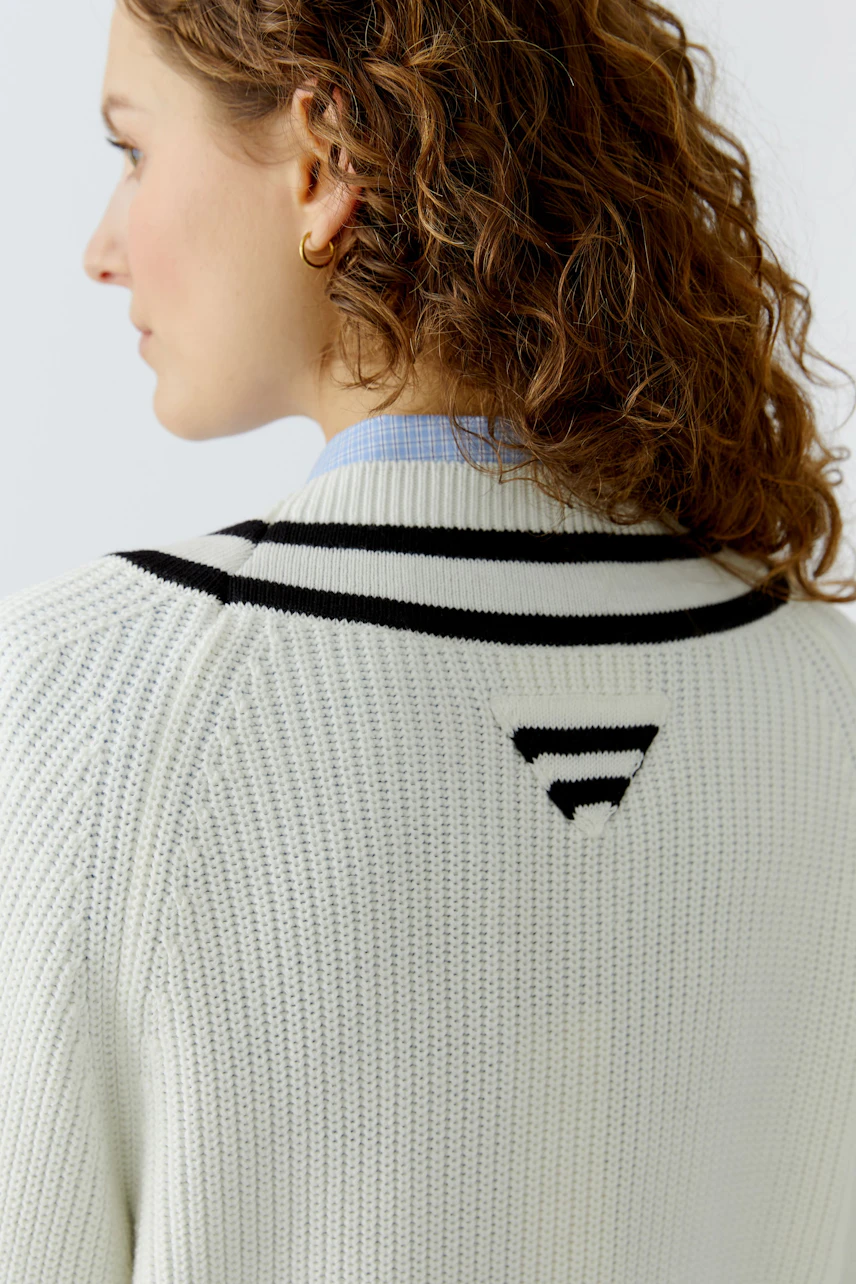 Casual women's pullover: A woman with curly hair wears a white knitted pullover with black stripes.